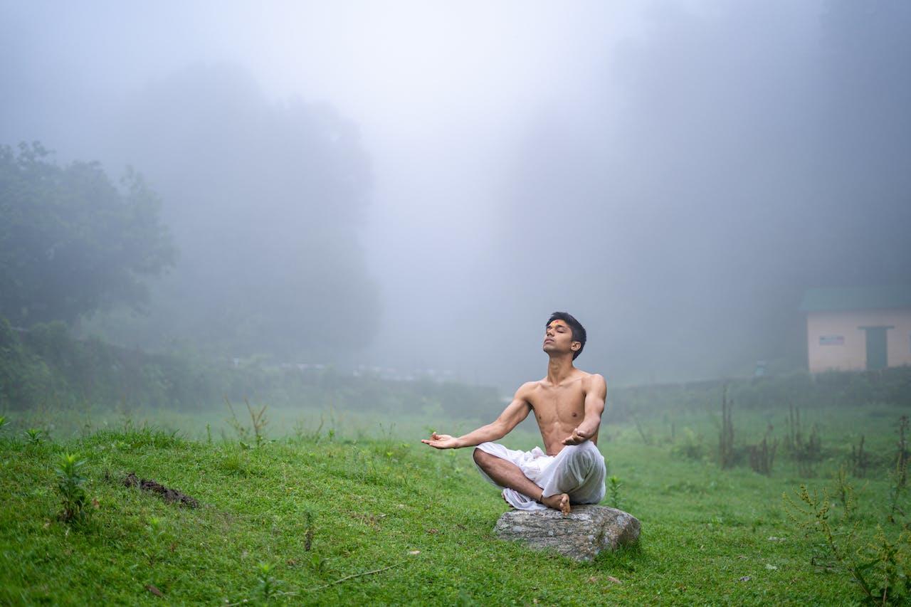 A man meditating on a rock in a field