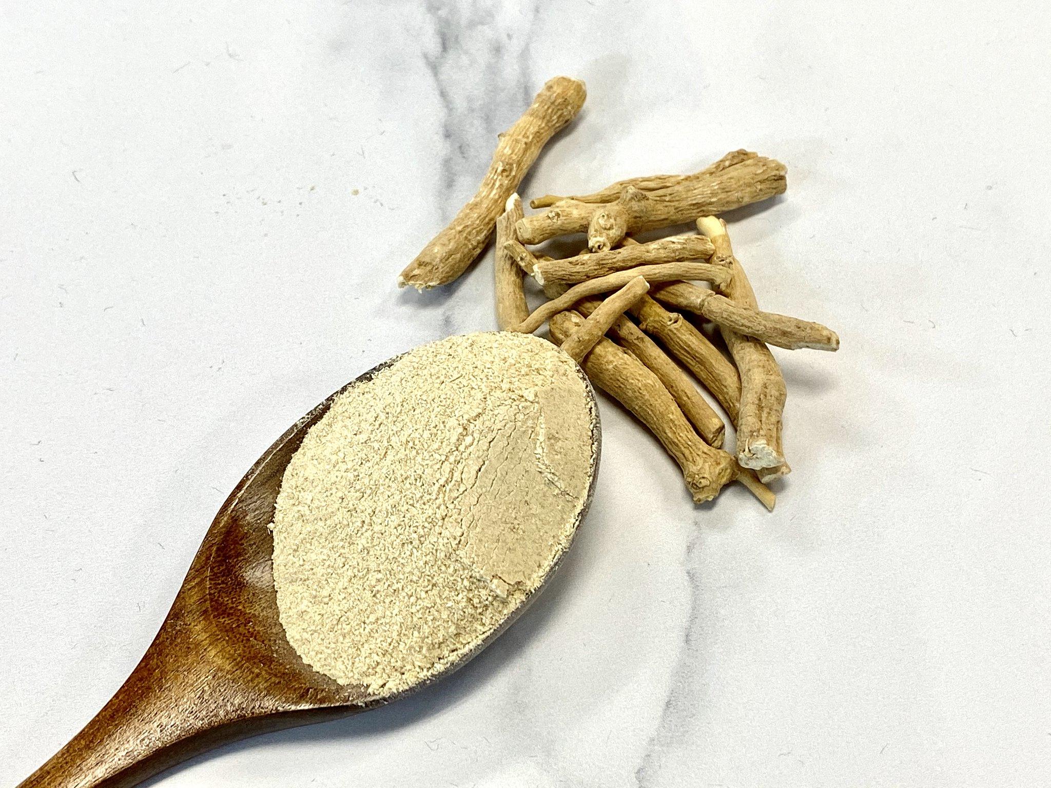 A wooden spoonful of powdered ashwagandha next to pieces of the whole root