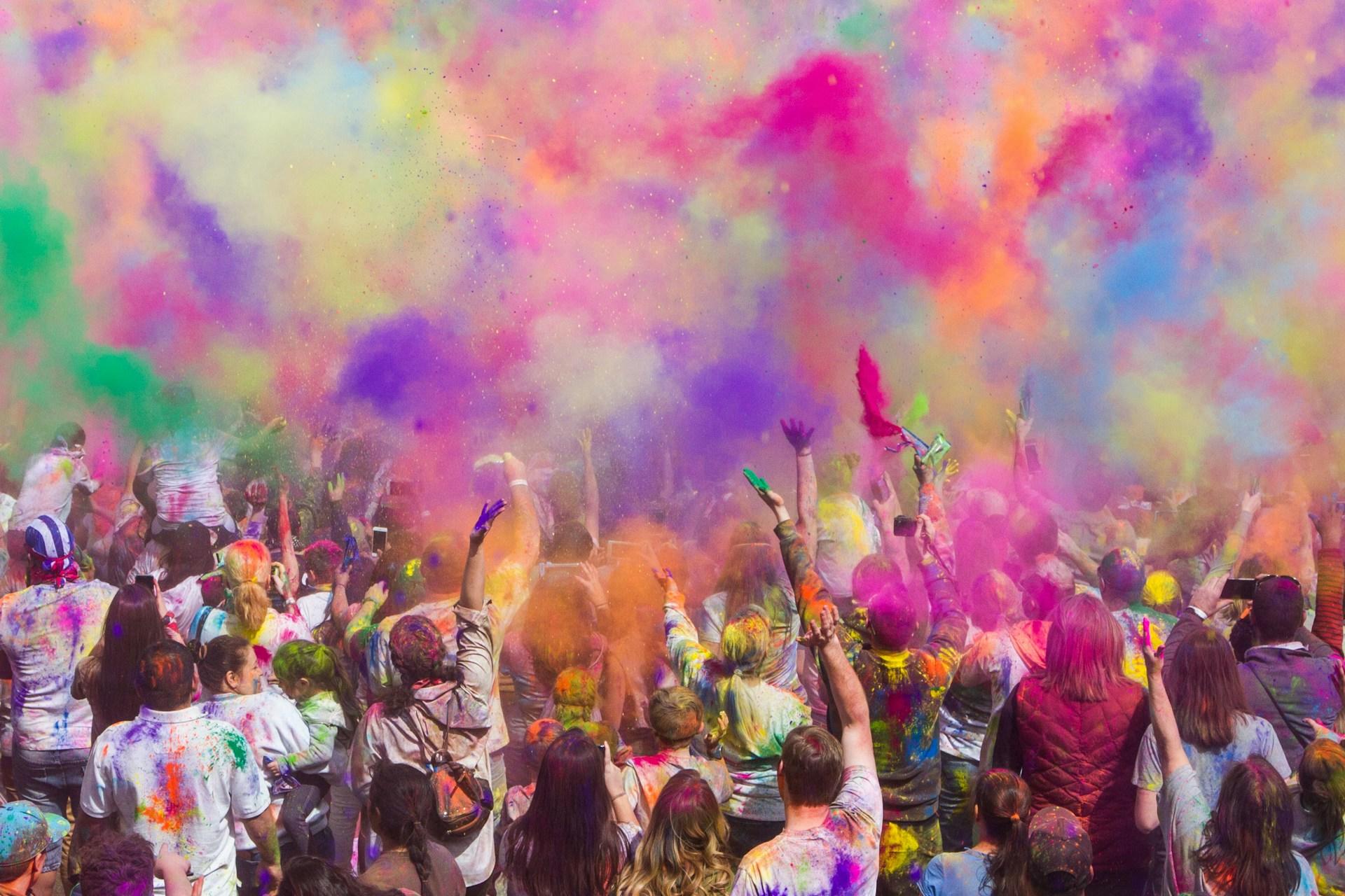 Dozens of people throwing Holi powder into the air at a festival