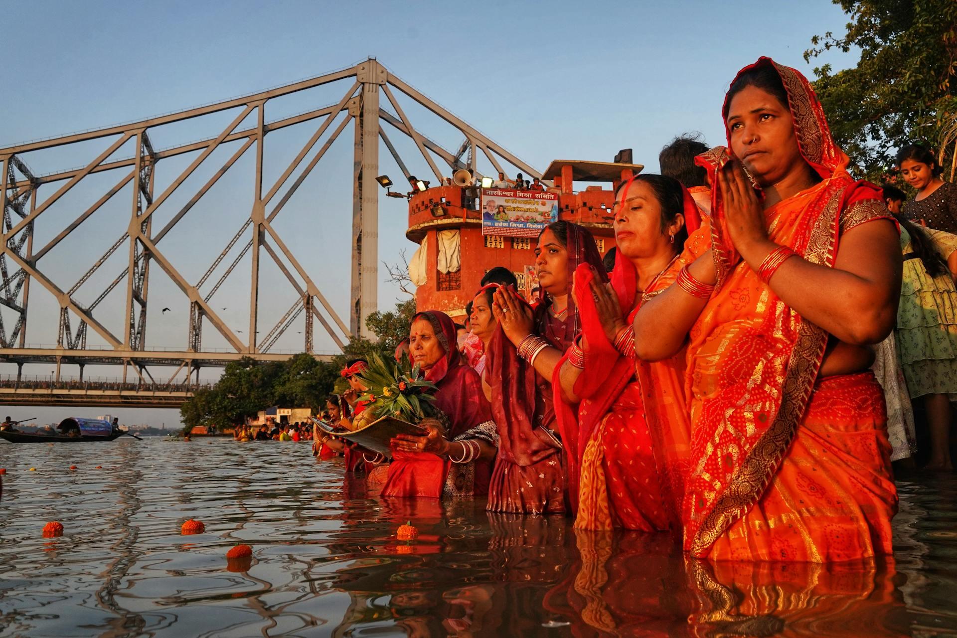 women in saree standing in a river, praying and holding offerings