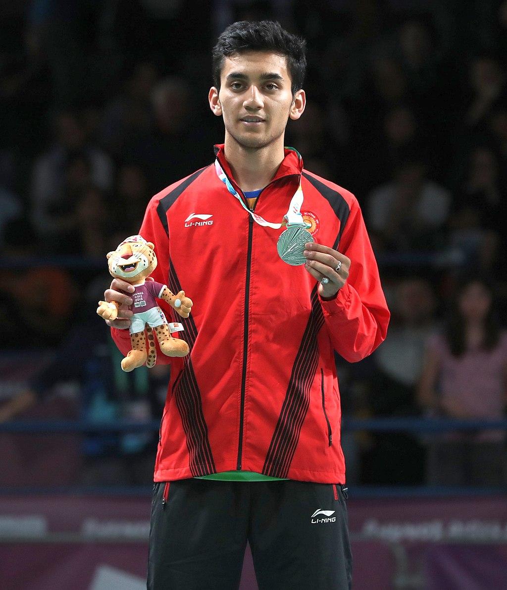Lakshya Sen wearing a gold medal around his neck and a mascot stuffed animal in one hand