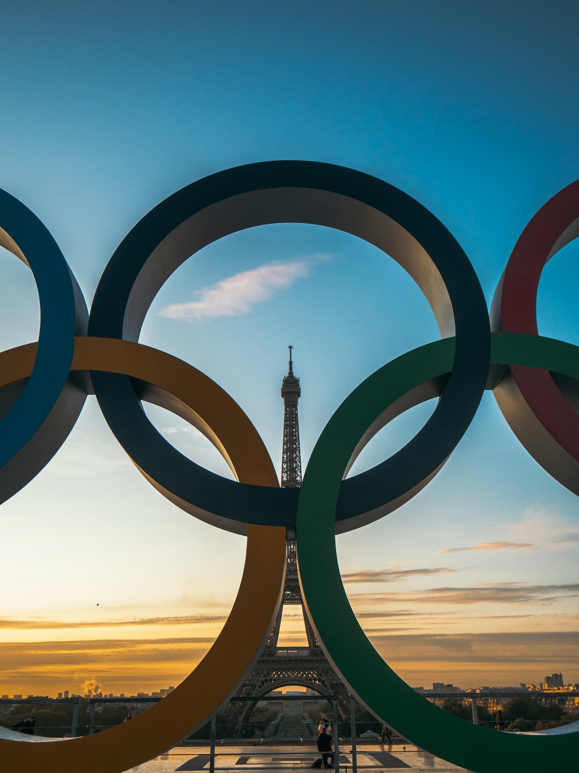 A photo of the Eiffel Tower as seen through the Olympic Ring statue nearby