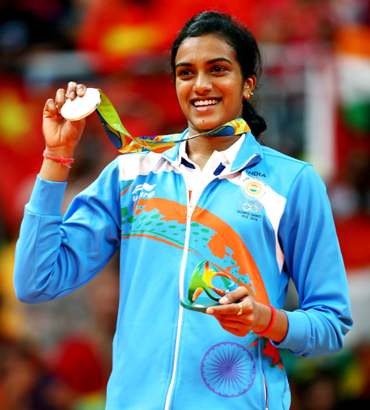 PV Sindhu wearing a silver medal around her neck and holding it up, while wearing her official Olympics sports gear