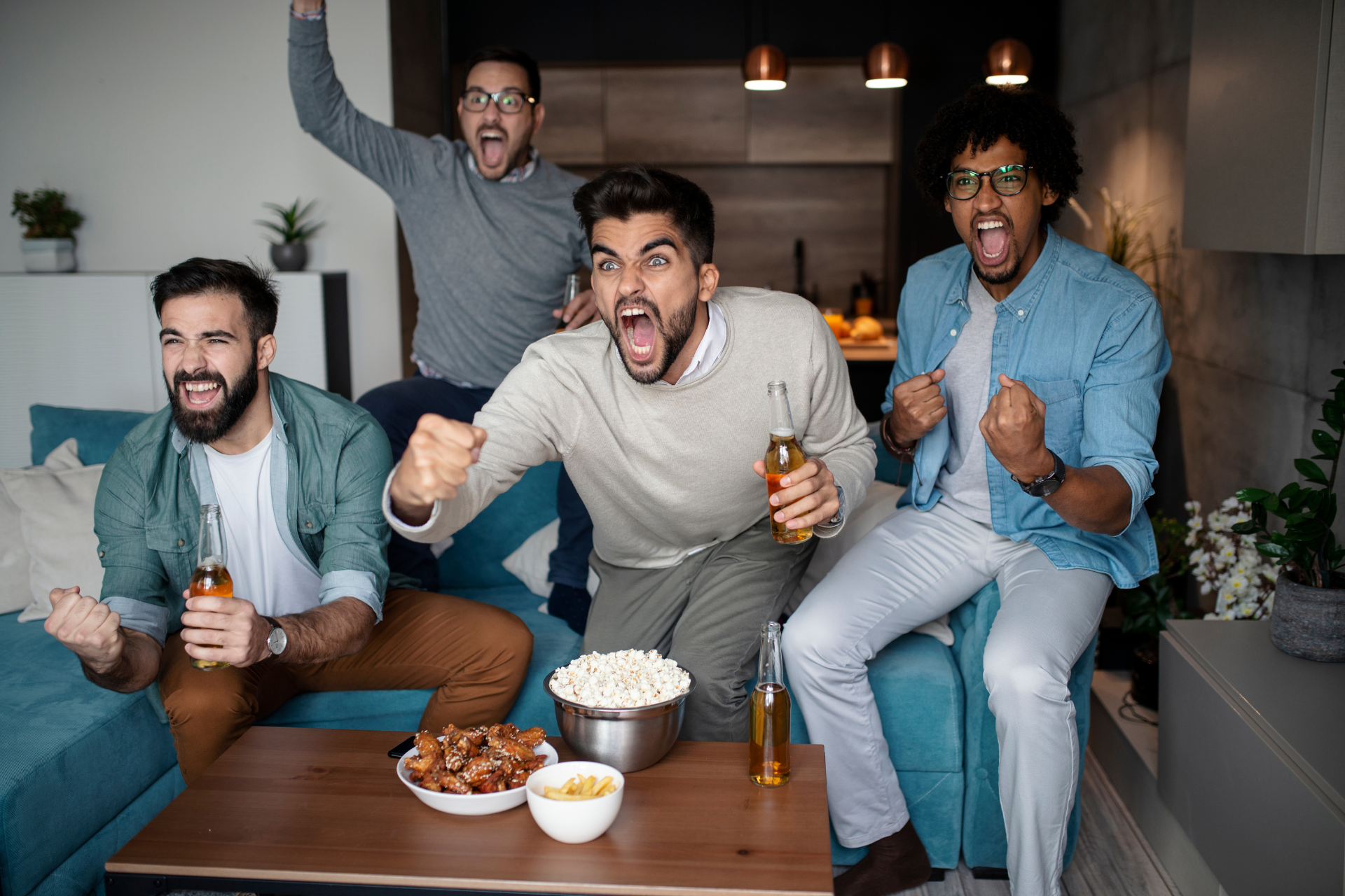 Four men at home with snacks watching TV and cheering at the screen