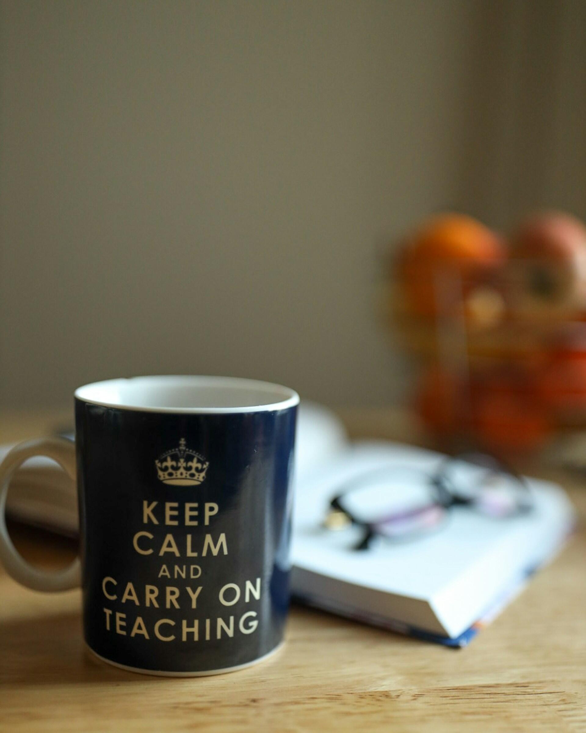 Tazza con la scritta “Keep Calm and Carry on Teaching” accanto a un quaderno.