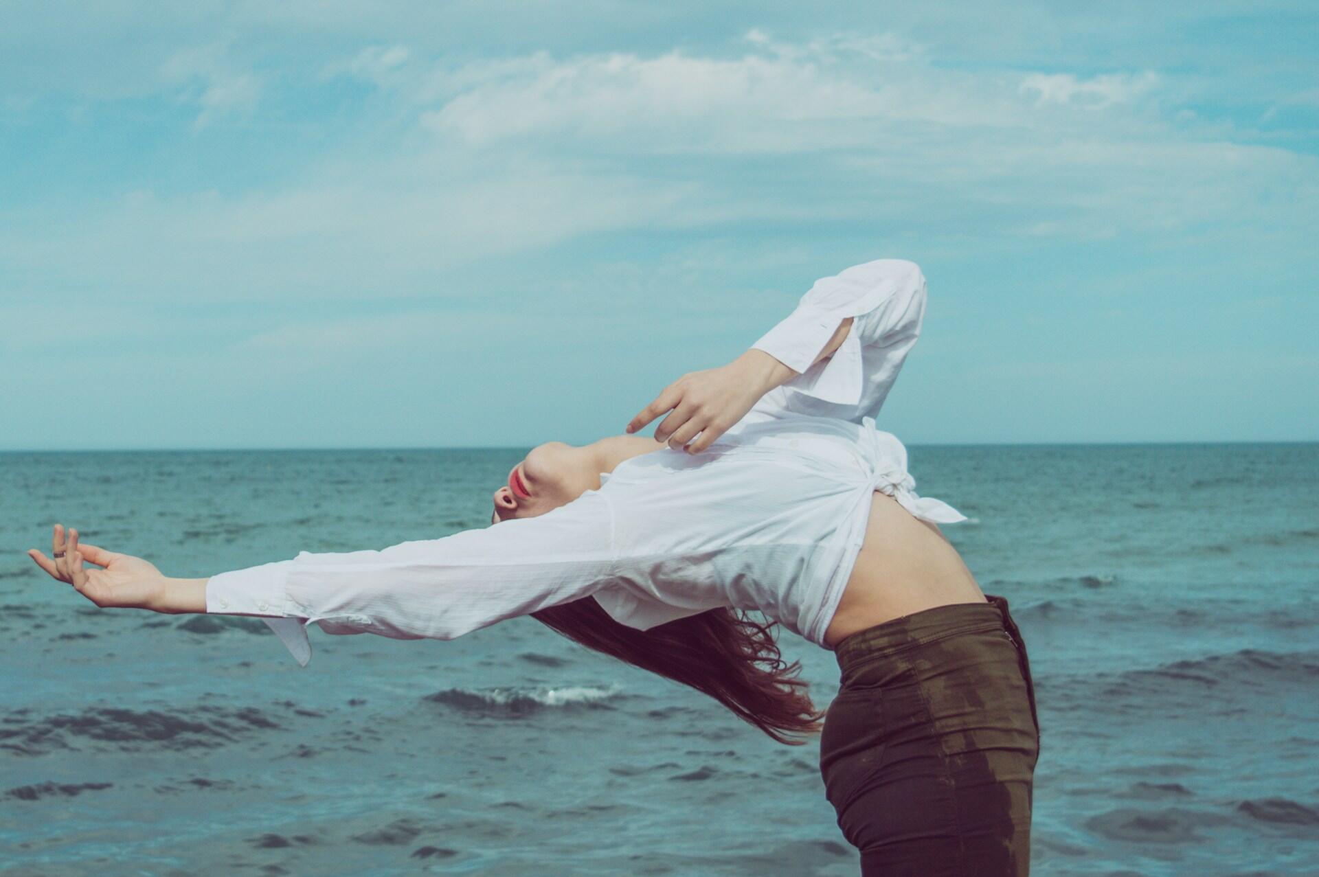 Una ragazza fa stretching per la schiena davanti al mare.