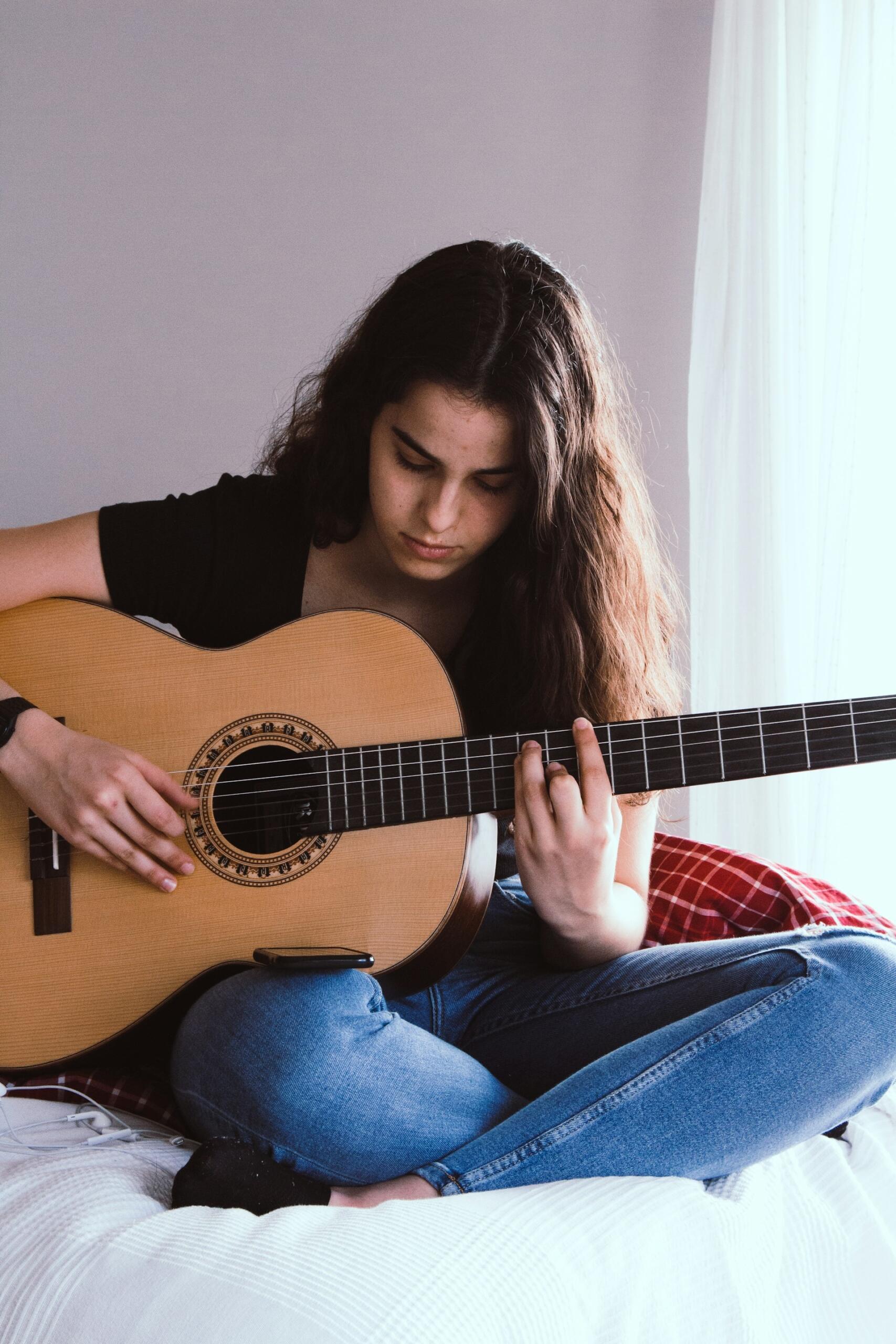 Ragazza prova accordi chitarra nella propria stanza.
