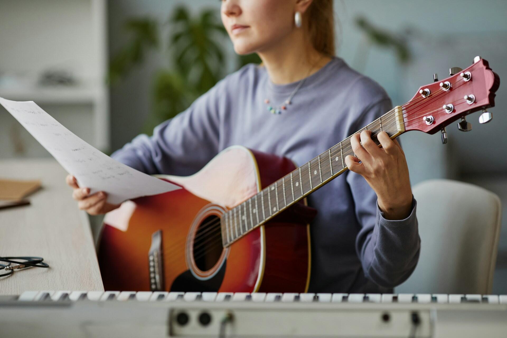 Ragazza studia chitarra leggendo un foglio con accordi.