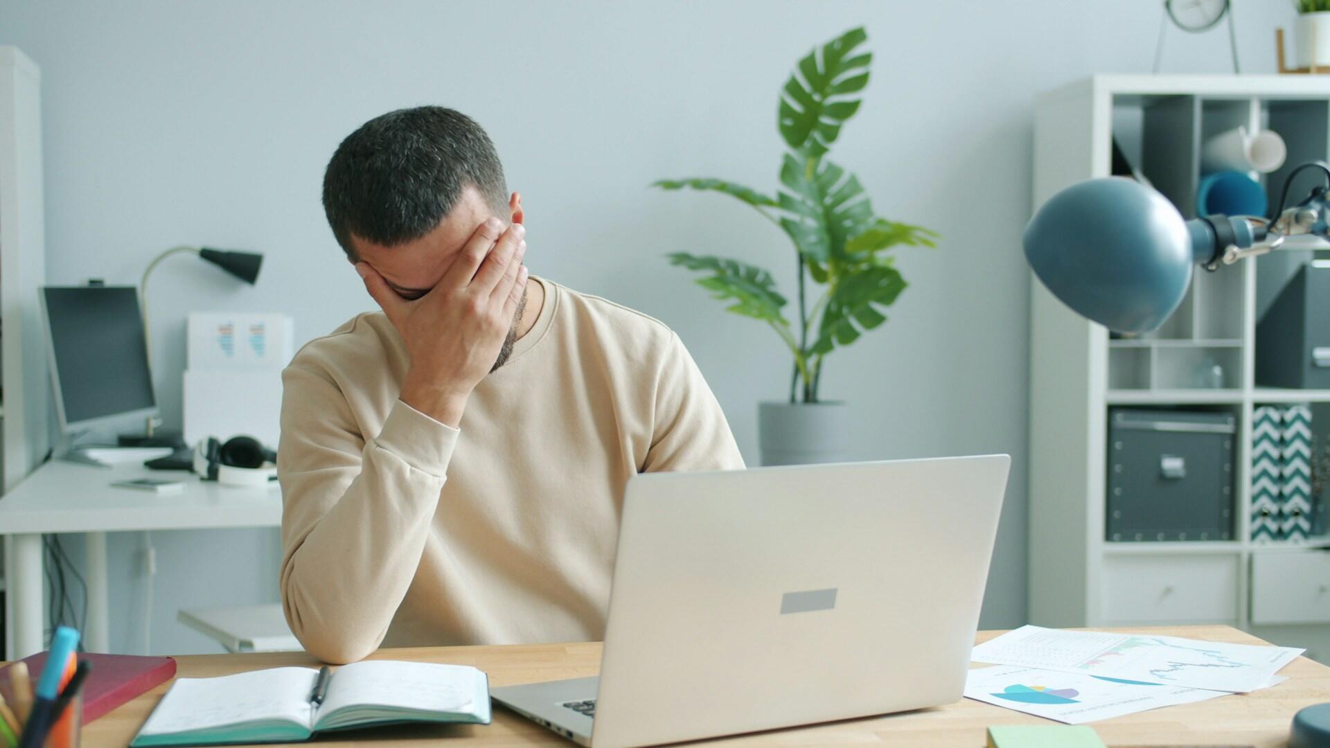 Ragazzo davanti al computer si copre il viso con una mano.