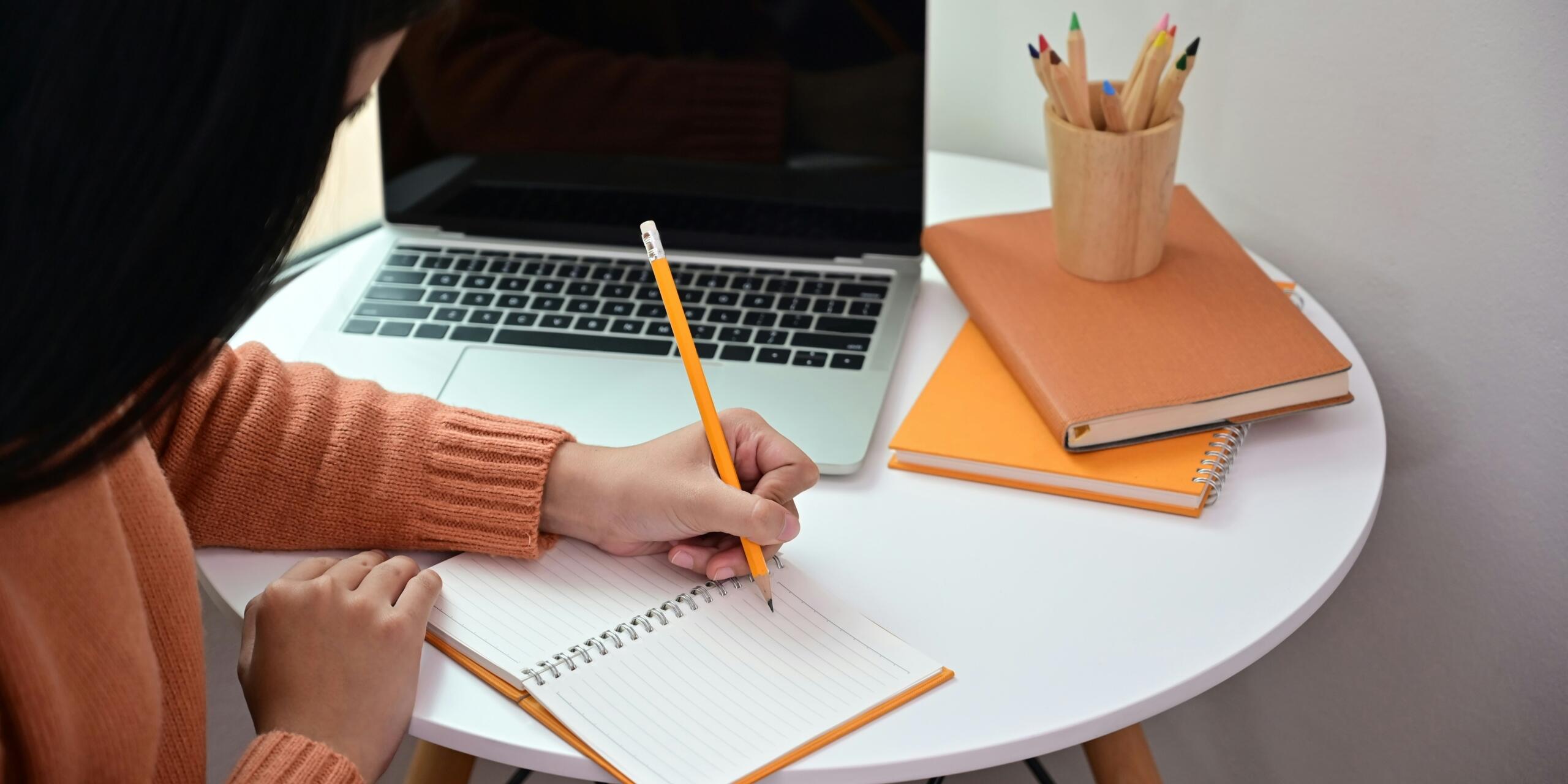 Ragazza Scrive con la matita sul quaderno vicino al pc.