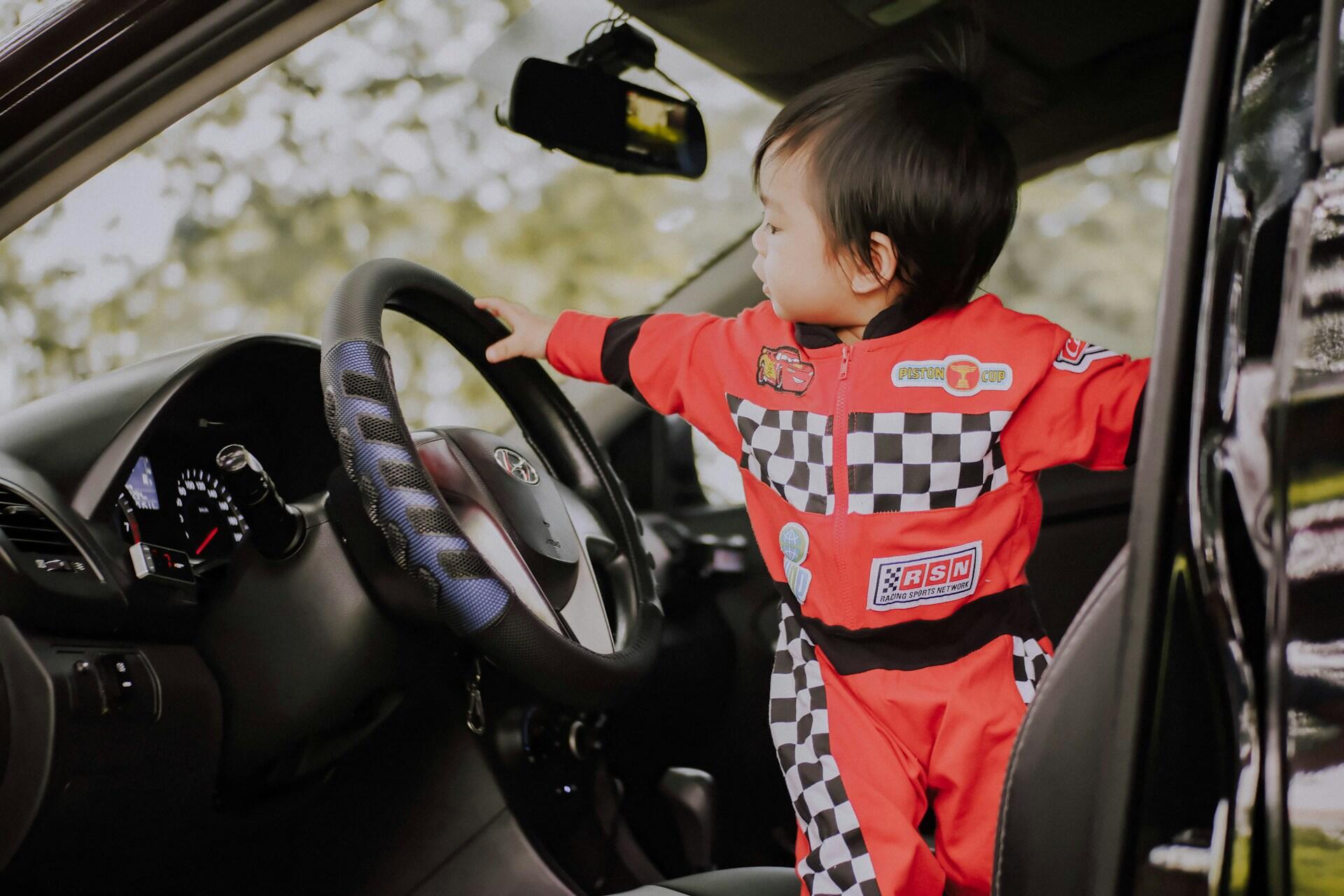 Bambino vestito da pilota tocca il volante di un auto.