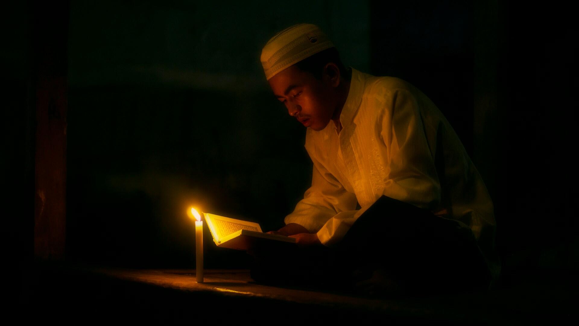 Devoto musulmano legge il Coranoa lume di candela dopo il digiuno del Ramadan.