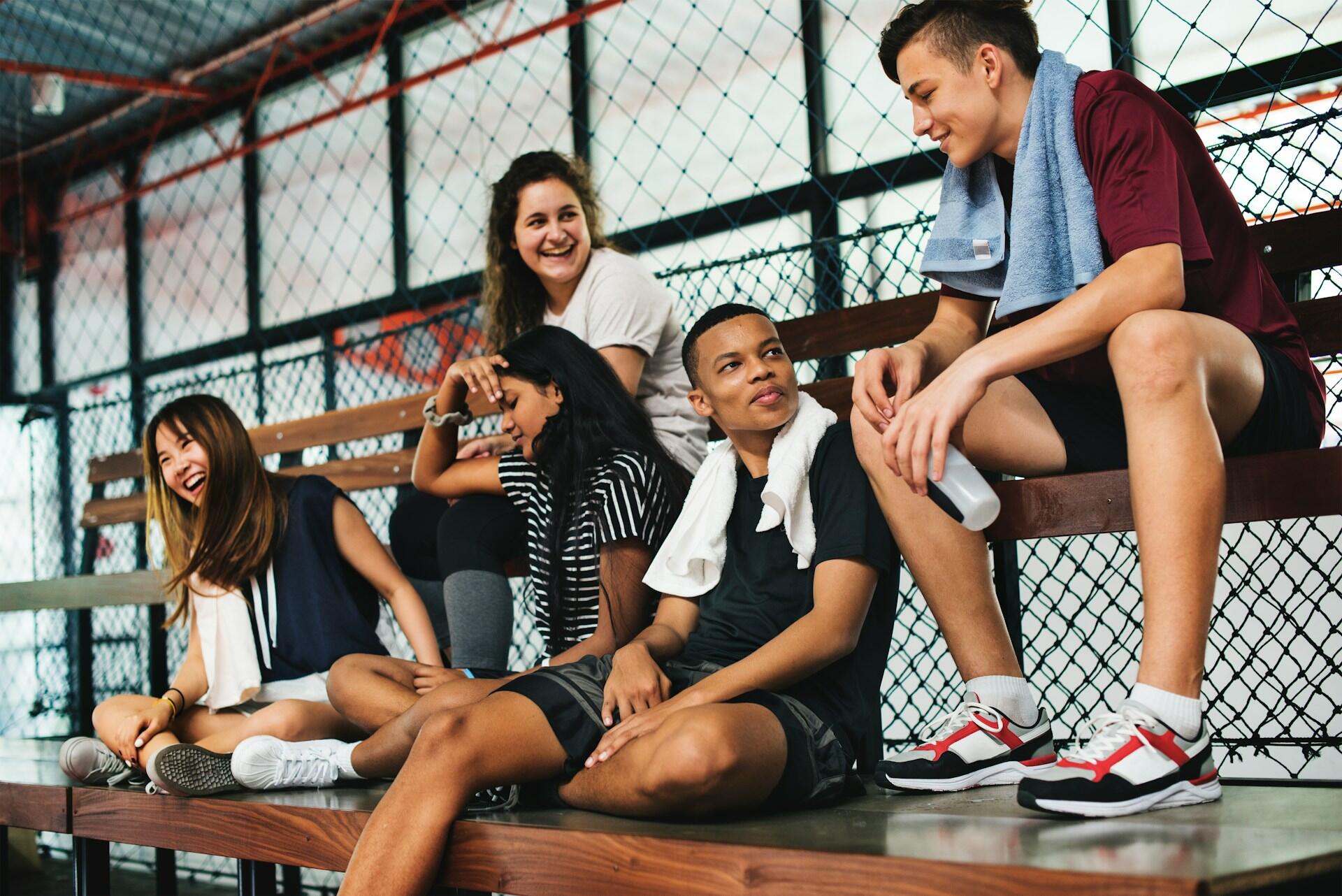Un gruppo di adolescenti seduti sulle panchine di una palestra dopo una partita. 