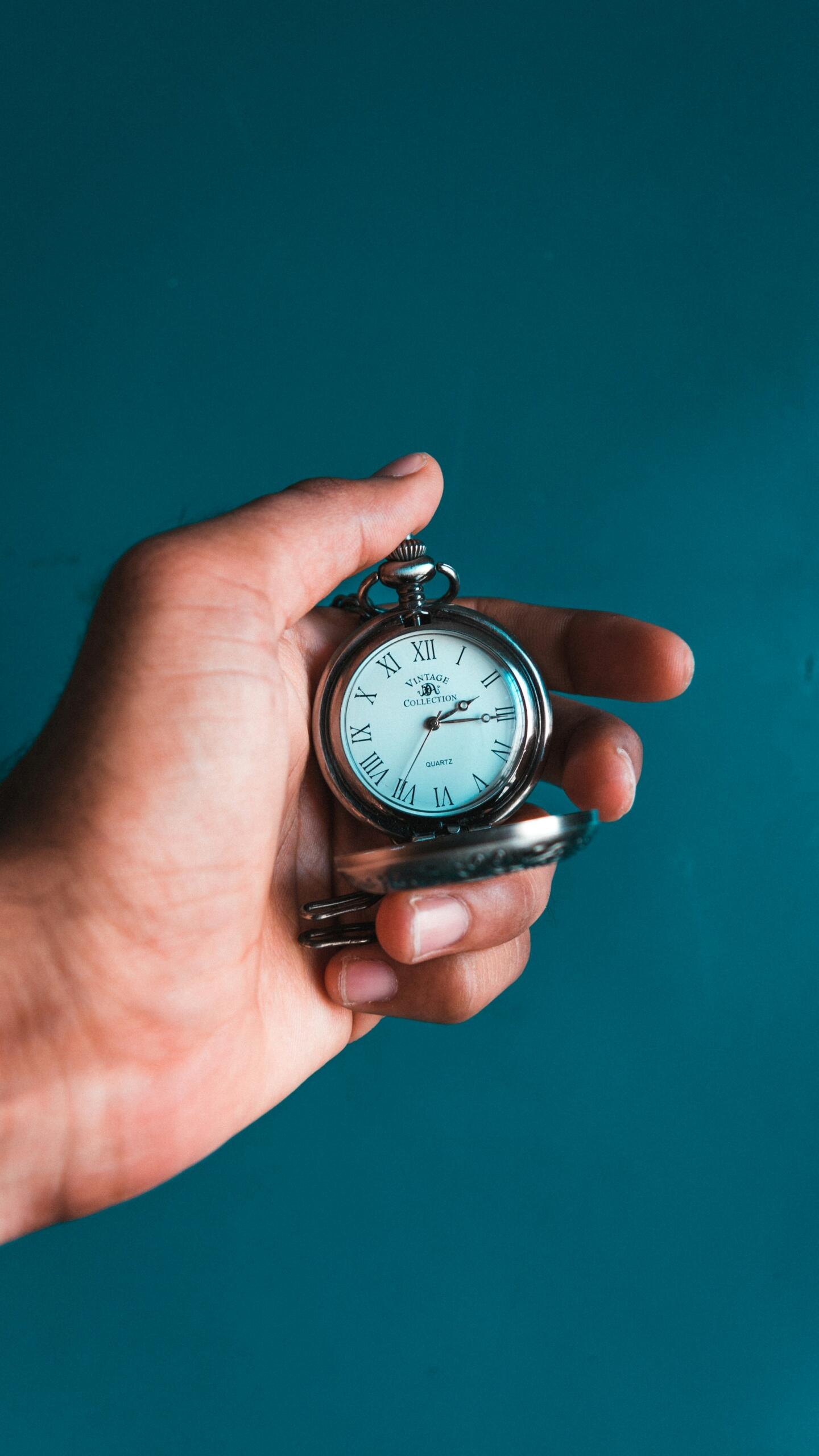 Un orologio da taschino tenuto in mano su sfondo blu. 