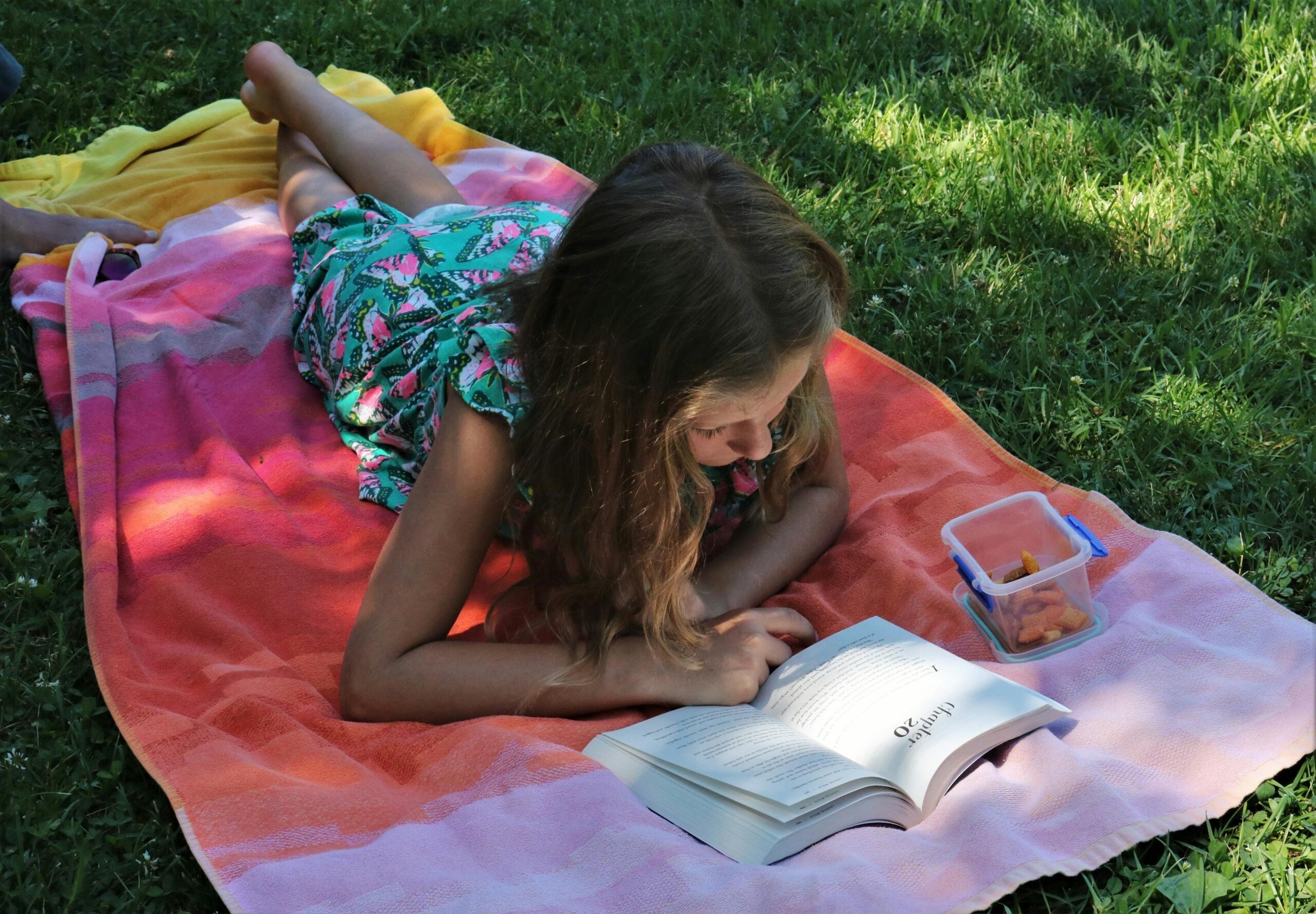 Bambina legge un libro sdraiata all'aperto.