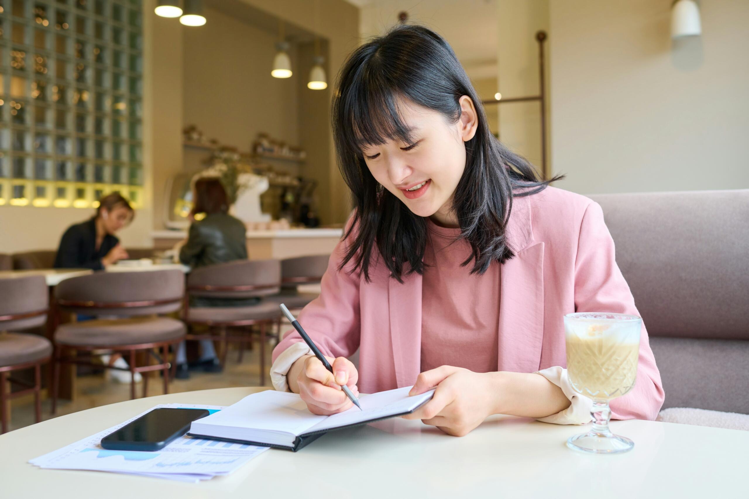 Ragazza scrive sul suo quaderno mentre è al bar.