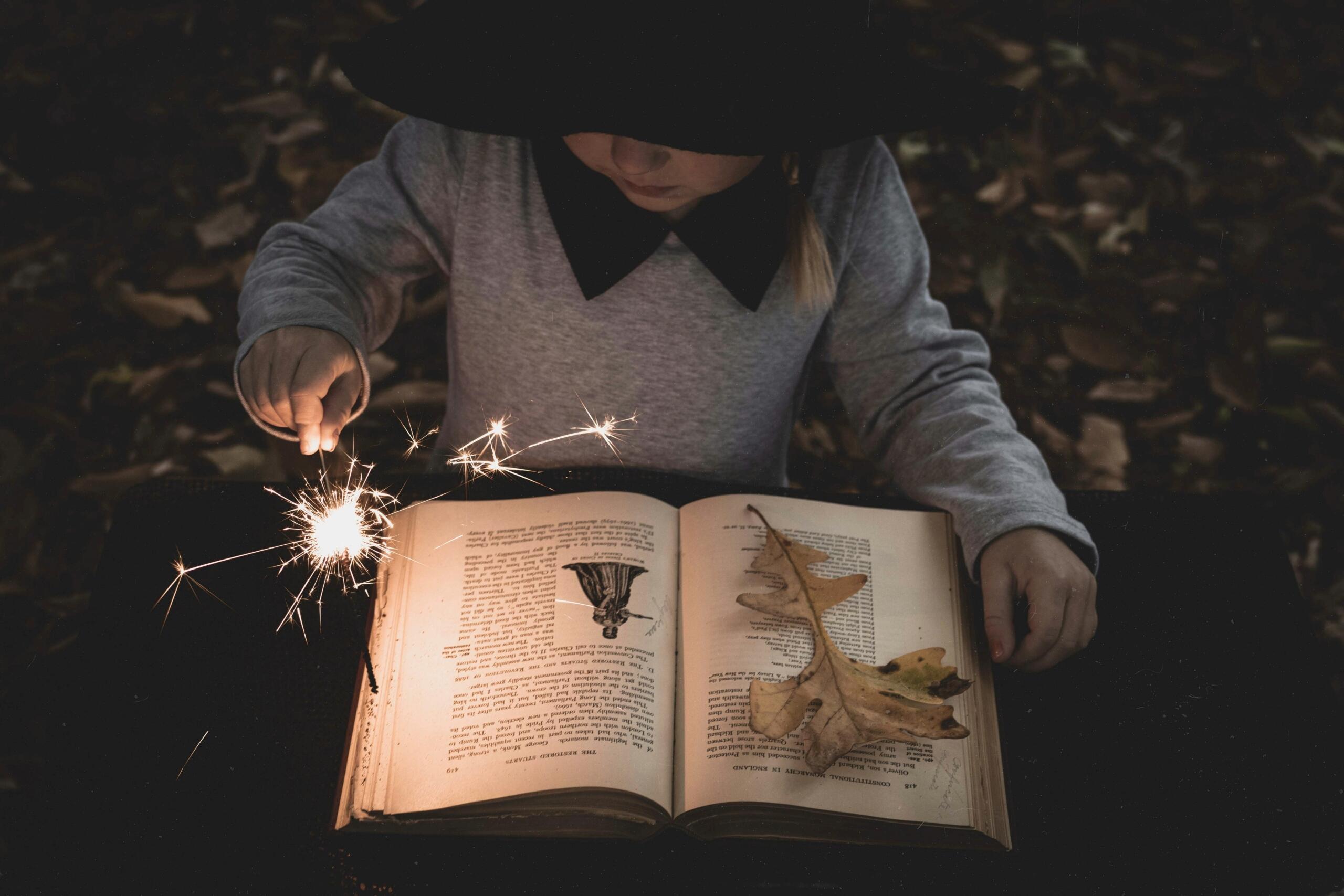 Bambina con un cappello da strega legge un libro in una foresta.