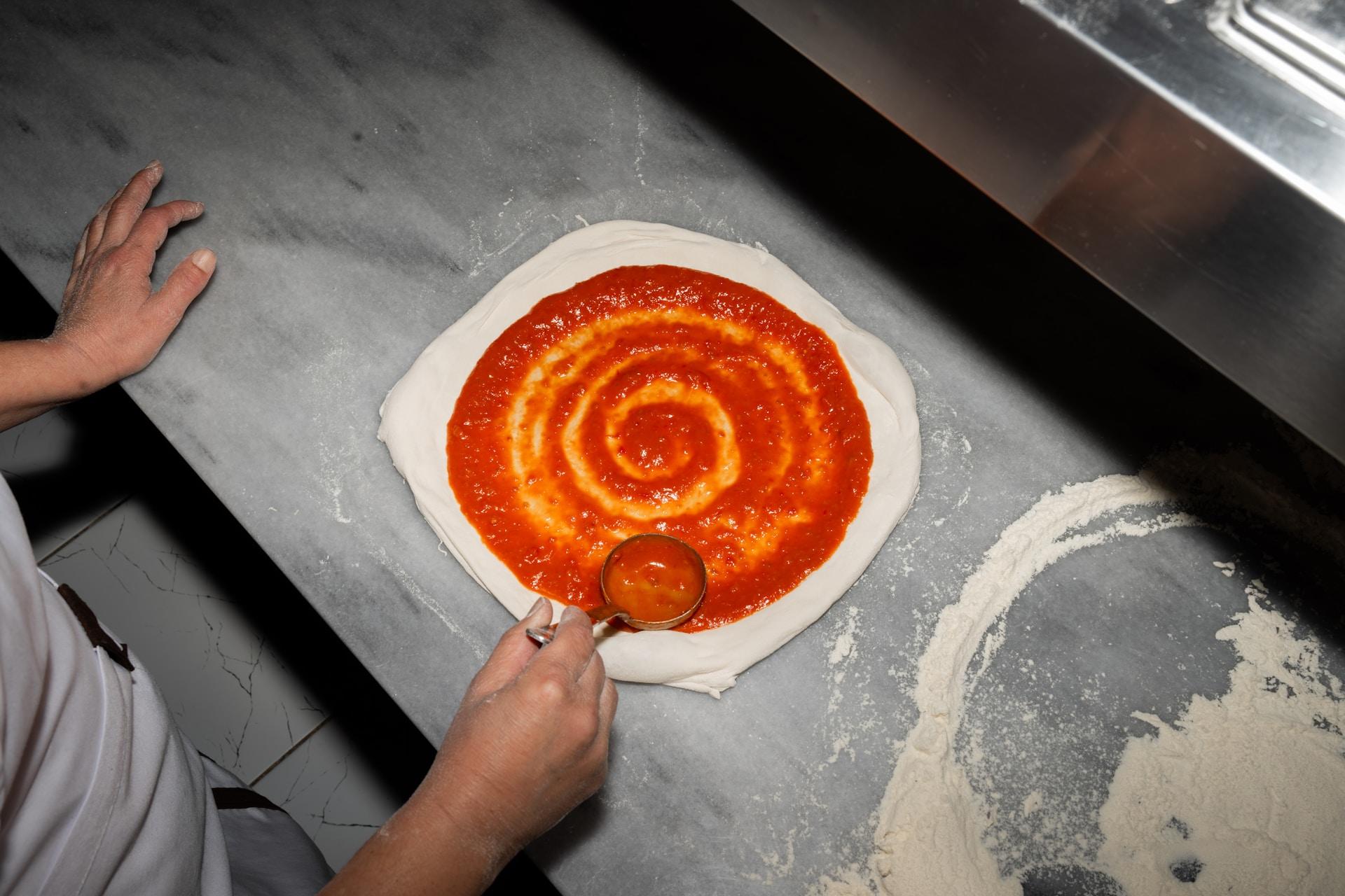 Pizzaiolo stende pomodoro sull'impasto 