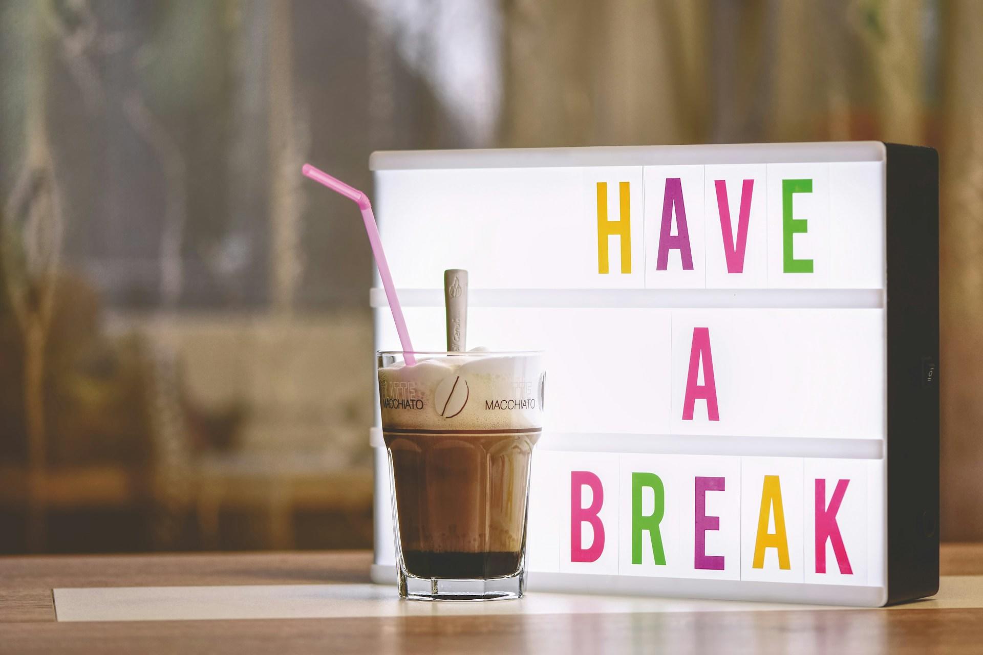 Cartello luminoso "Have a break" con caffè macchiato davanti