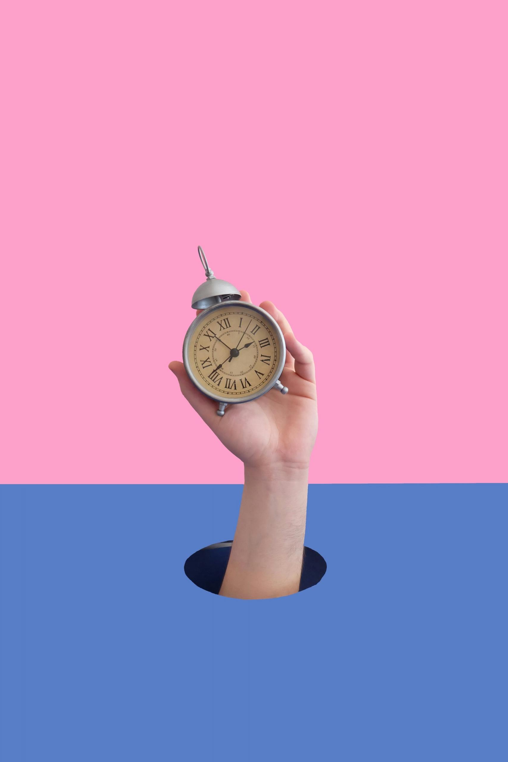 Mano che regge sveglia su blocco colore azzurro e rosa