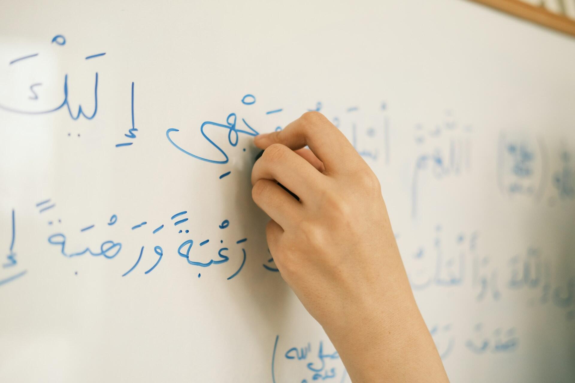 Insegnante scrive alla lavagna utilizzando l'alfabeto arabo.