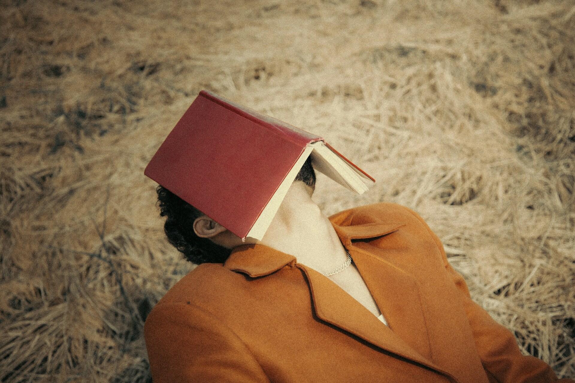 Un ragazzo tiene un libro aperto poggiato sulla faccia.