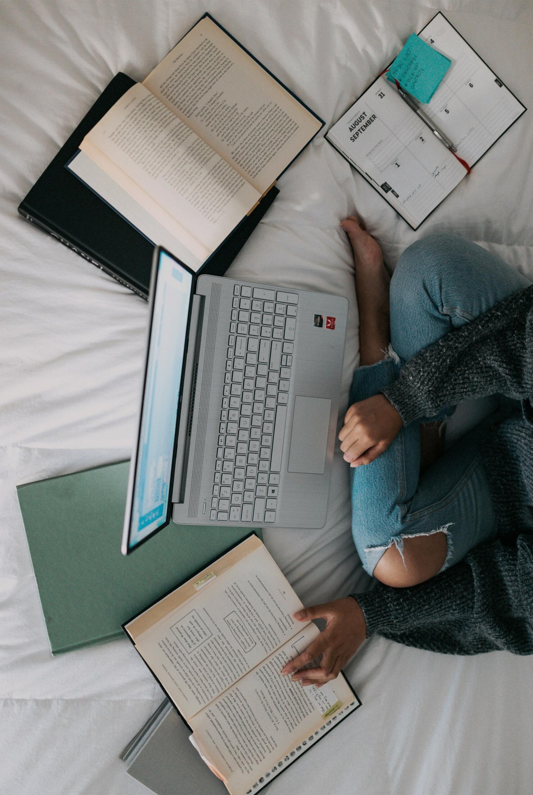 Una studentessa dei prepara all'esame di maturità sul letto con computer e diversi libri aperti.