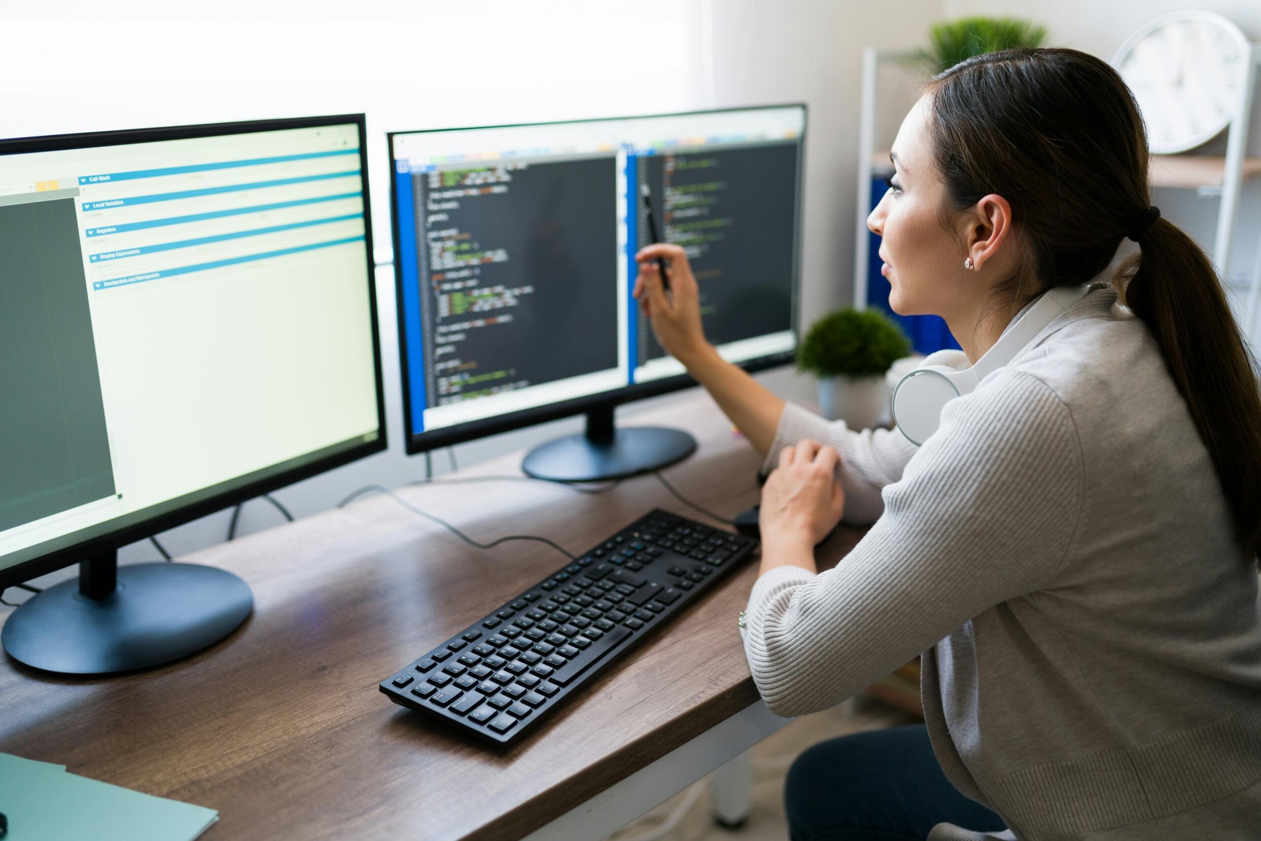 Donna al lavoro con due schermi e una tastiera.