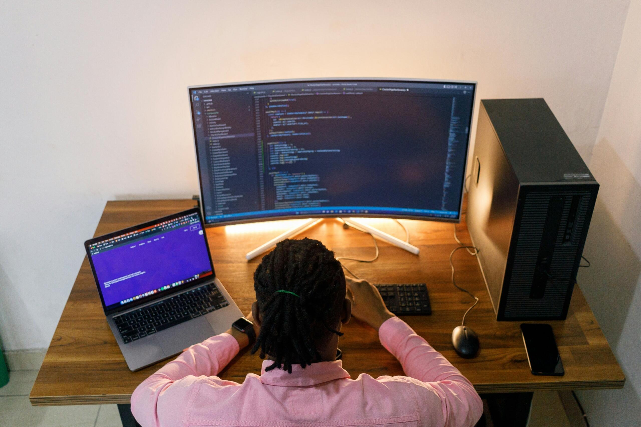 Persona di spalle alla scrivania che digita codice al pc.