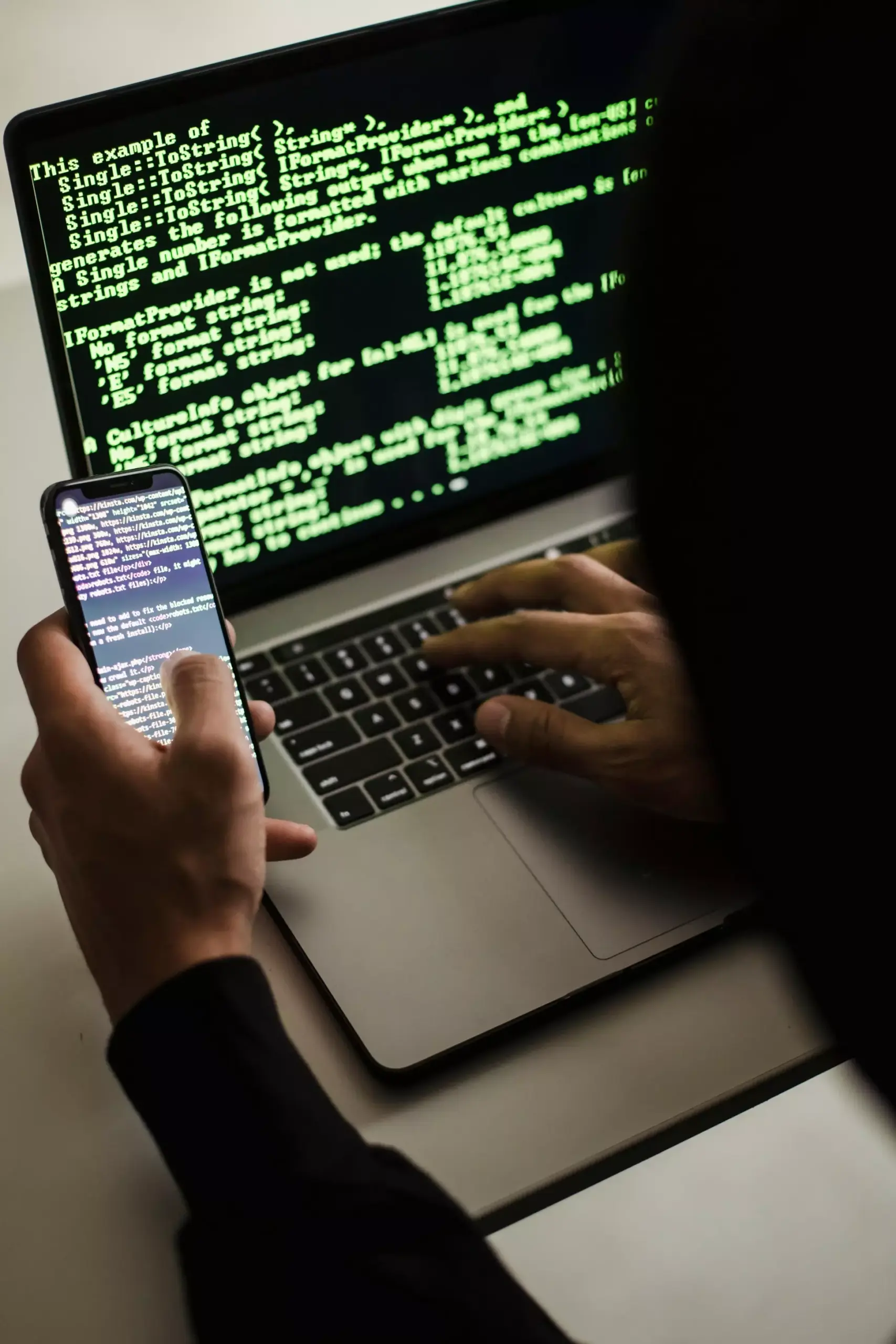 Persona che scrive sullo smartphone mentre digita al pc con schermo aperto sul terminale.