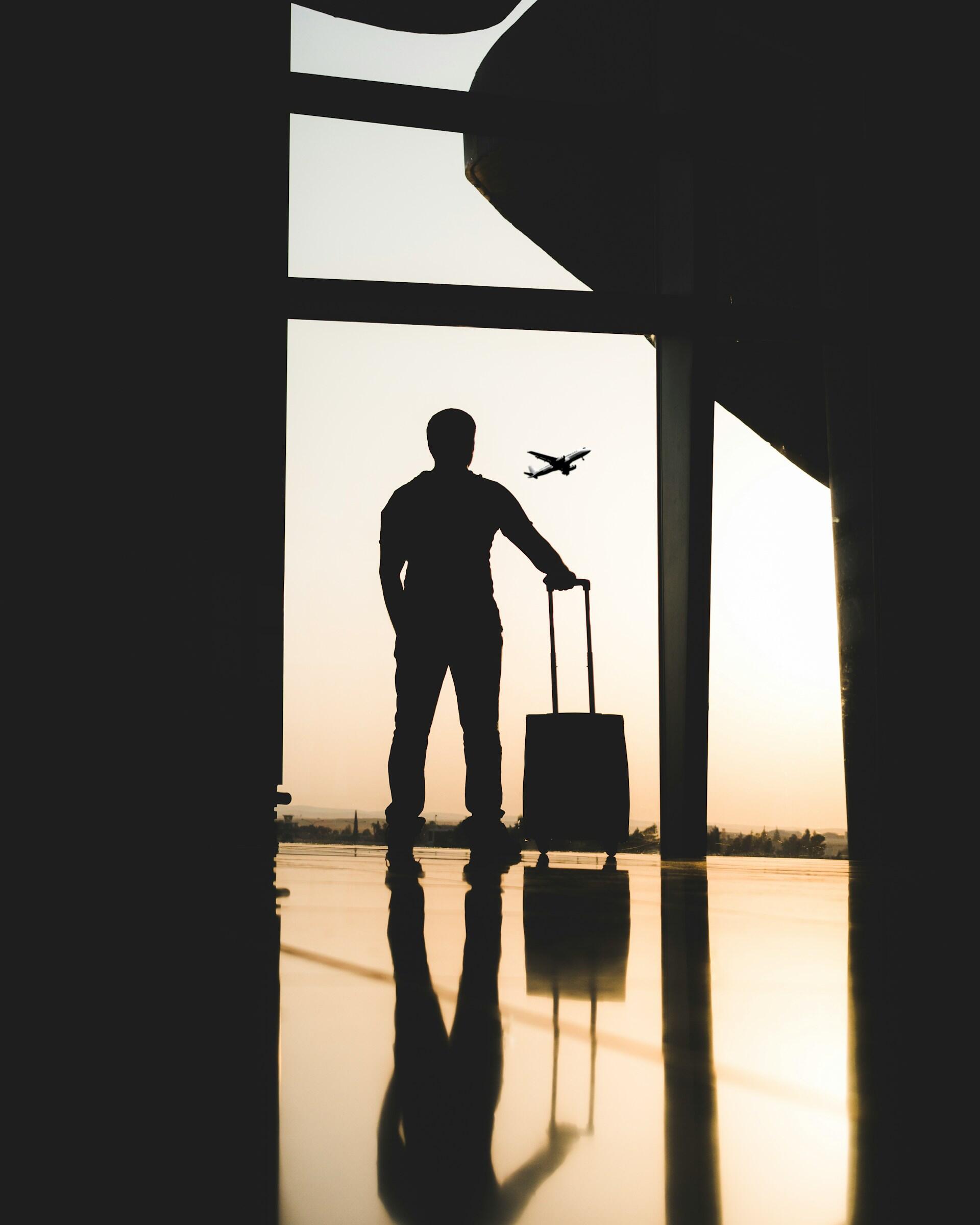 La sagoma di un uomo con una valigia in controluce nell'hangar di un aeroporto.
