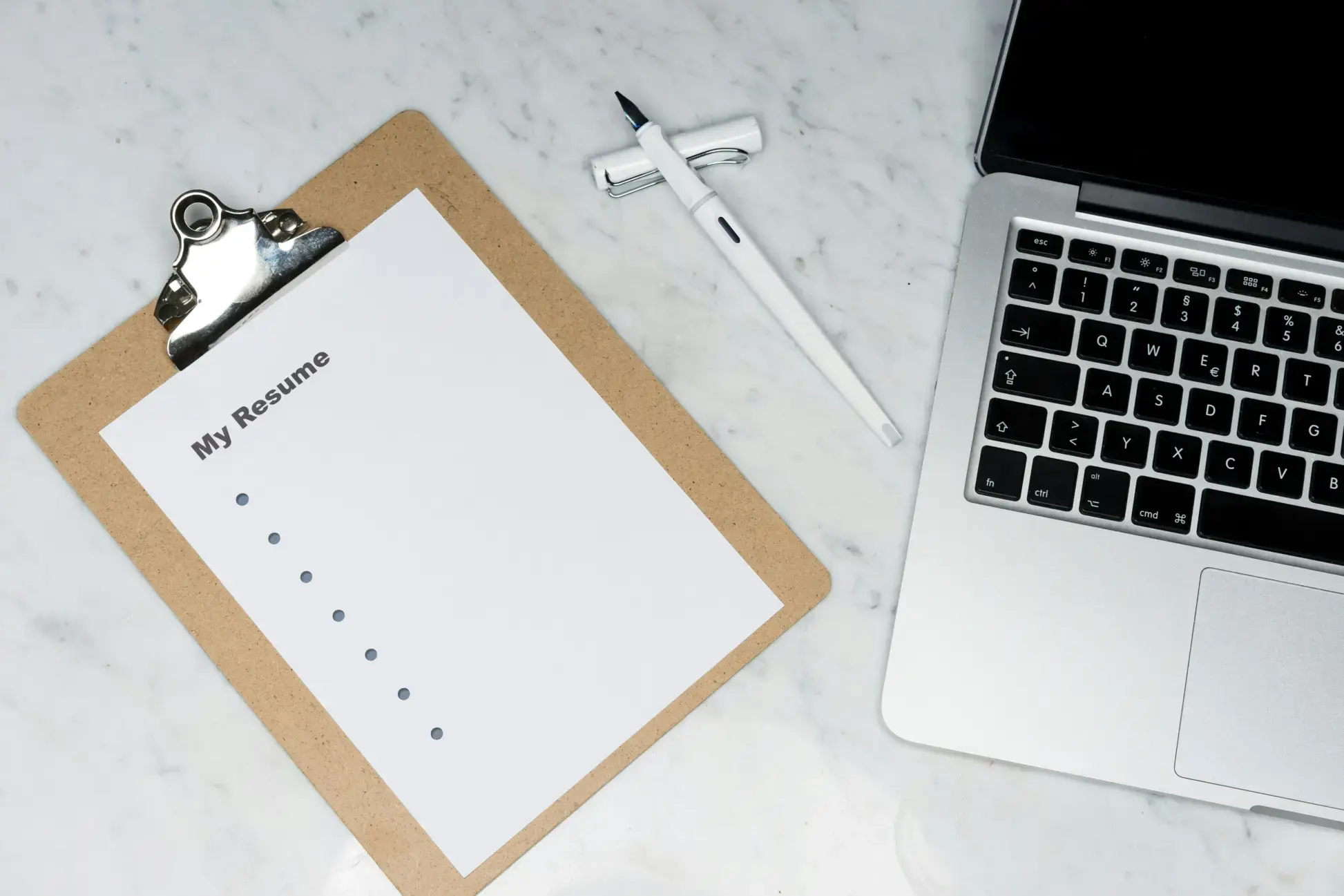 Un curriculum bianco intitolato «Il mio curriculum» su una clip board, accanto a un computer portatile e a una penna bianca, su una superficie di marmo.
