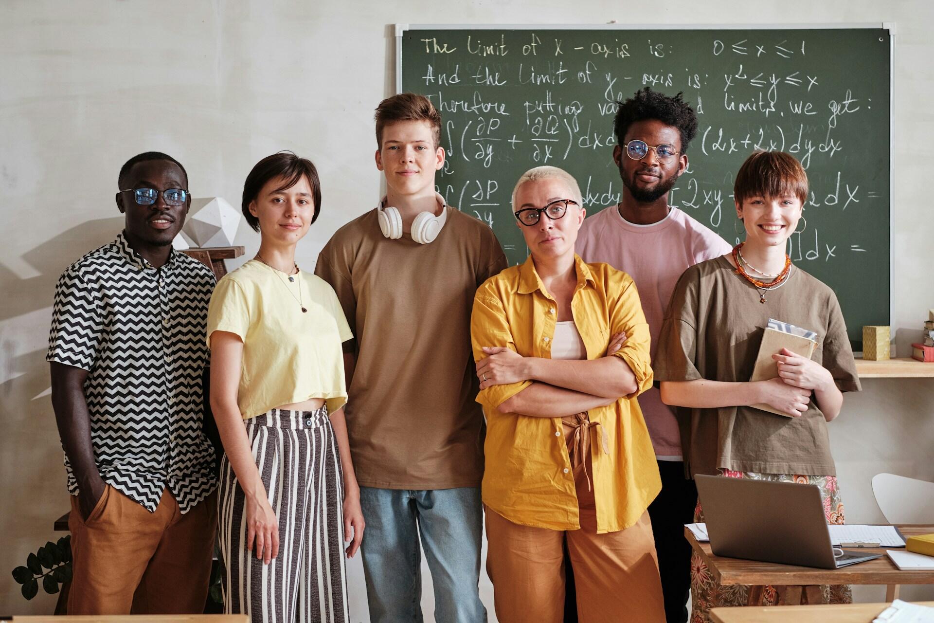 Gruppo di giovani universitari e docente davanti a una lavagna con formule matematiche.