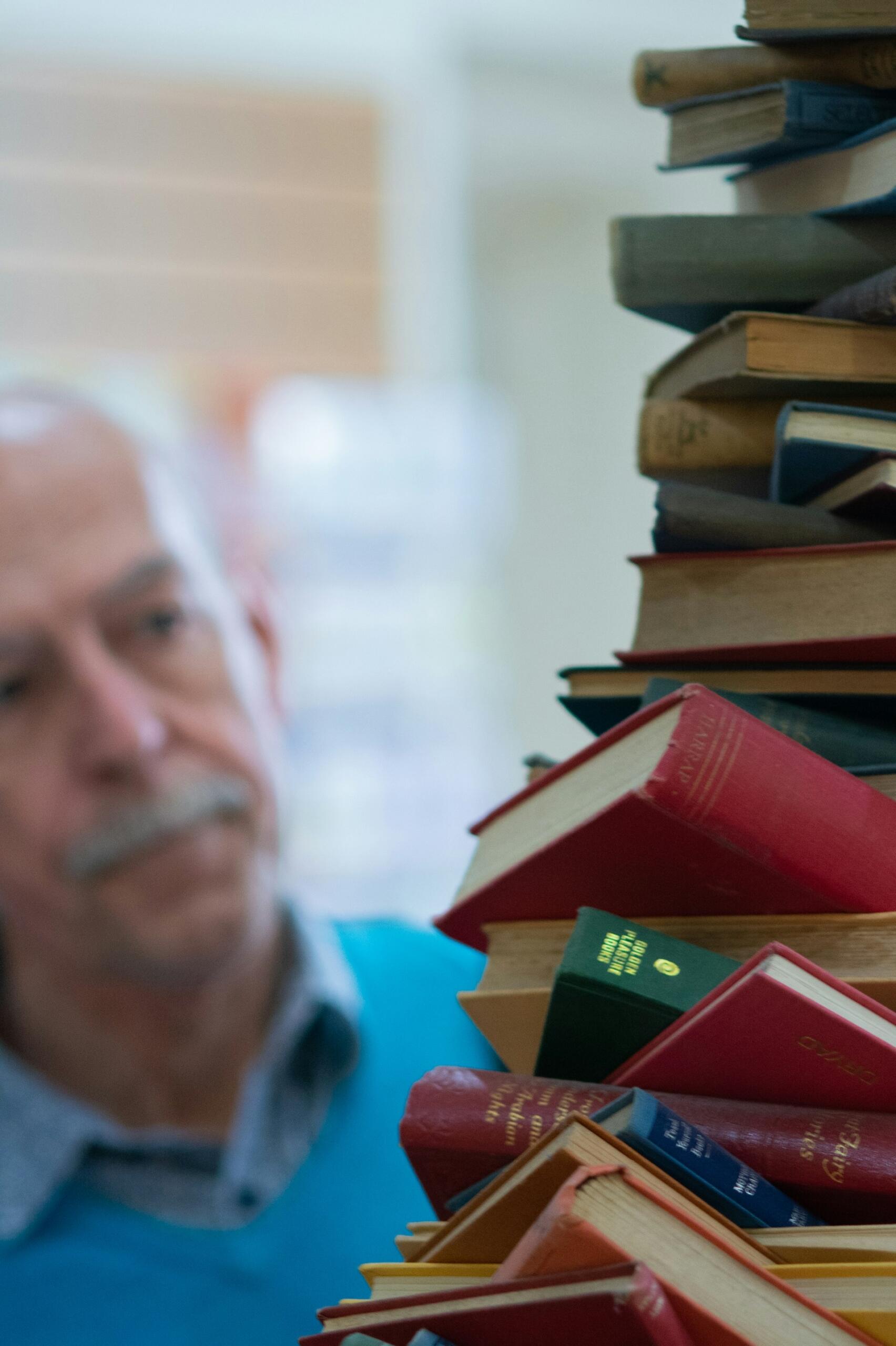 Professore universitario anziano dietro una pila di libri accademici.