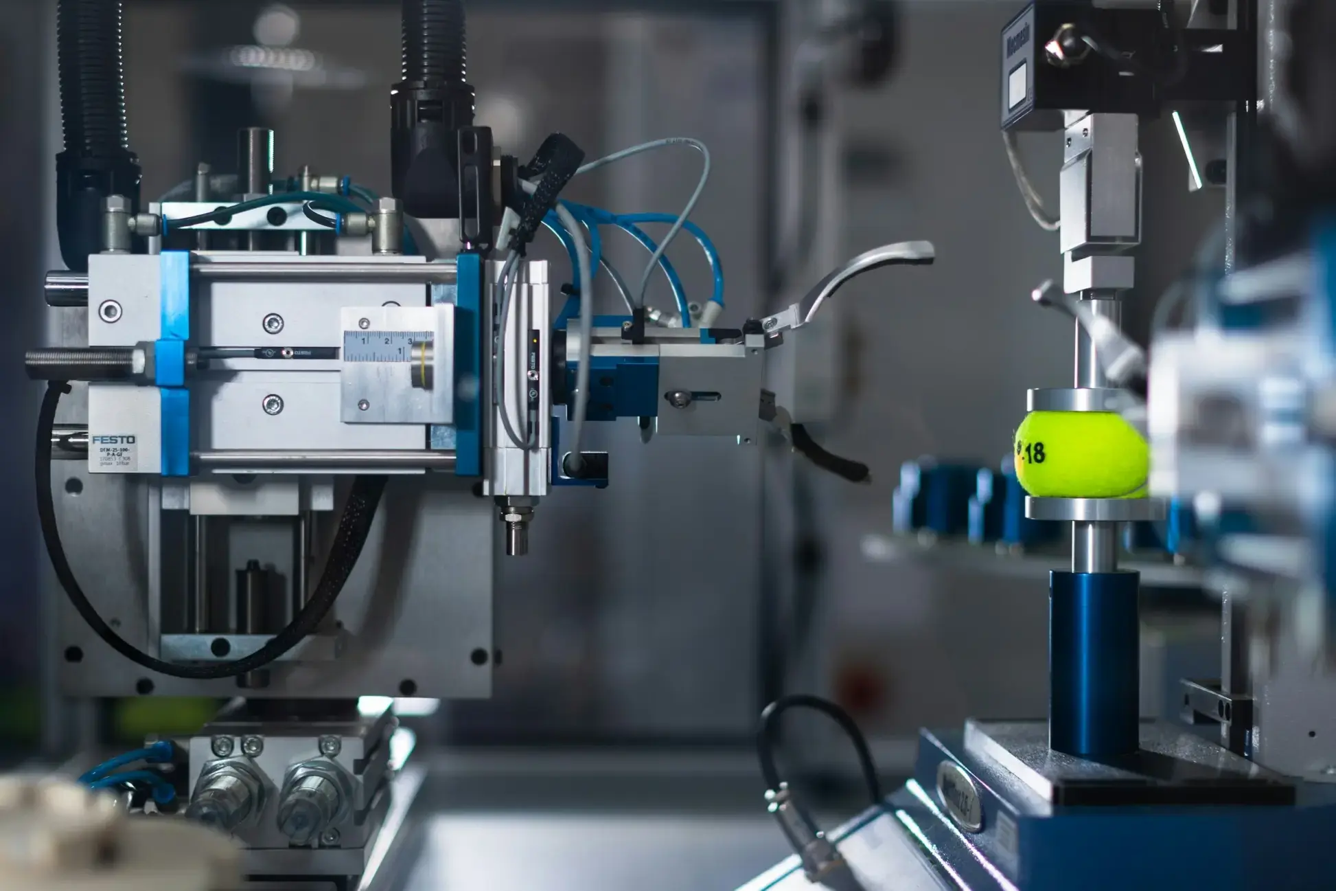 Primo piano di una macchina automatizzata che tiene una pallina da tennis gialla, in cui si distinguono i componenti e i controlli di ingegneria di precisione.