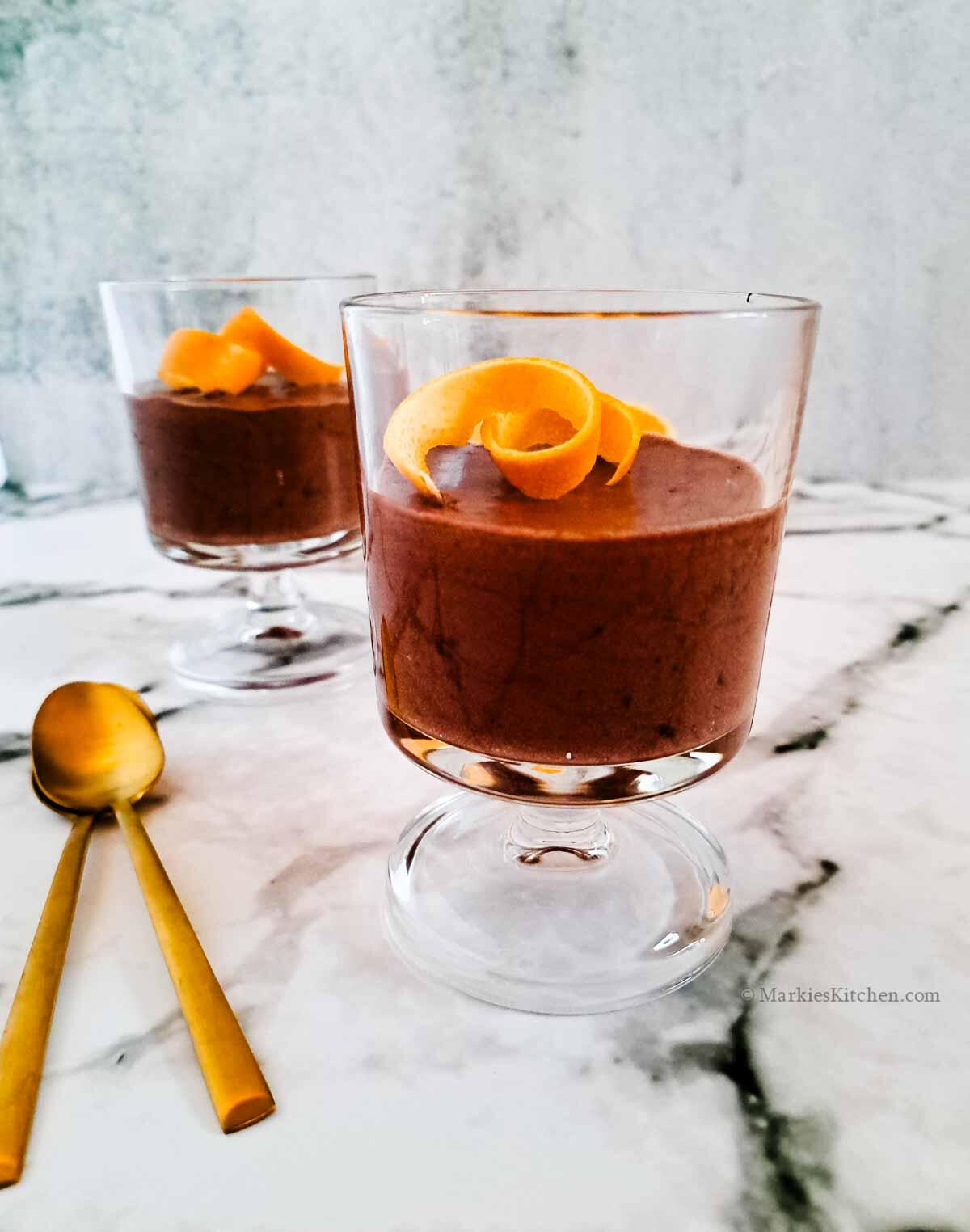 Bicchieri con mousse al cioccolato e arancia con cucchiaini dorati.