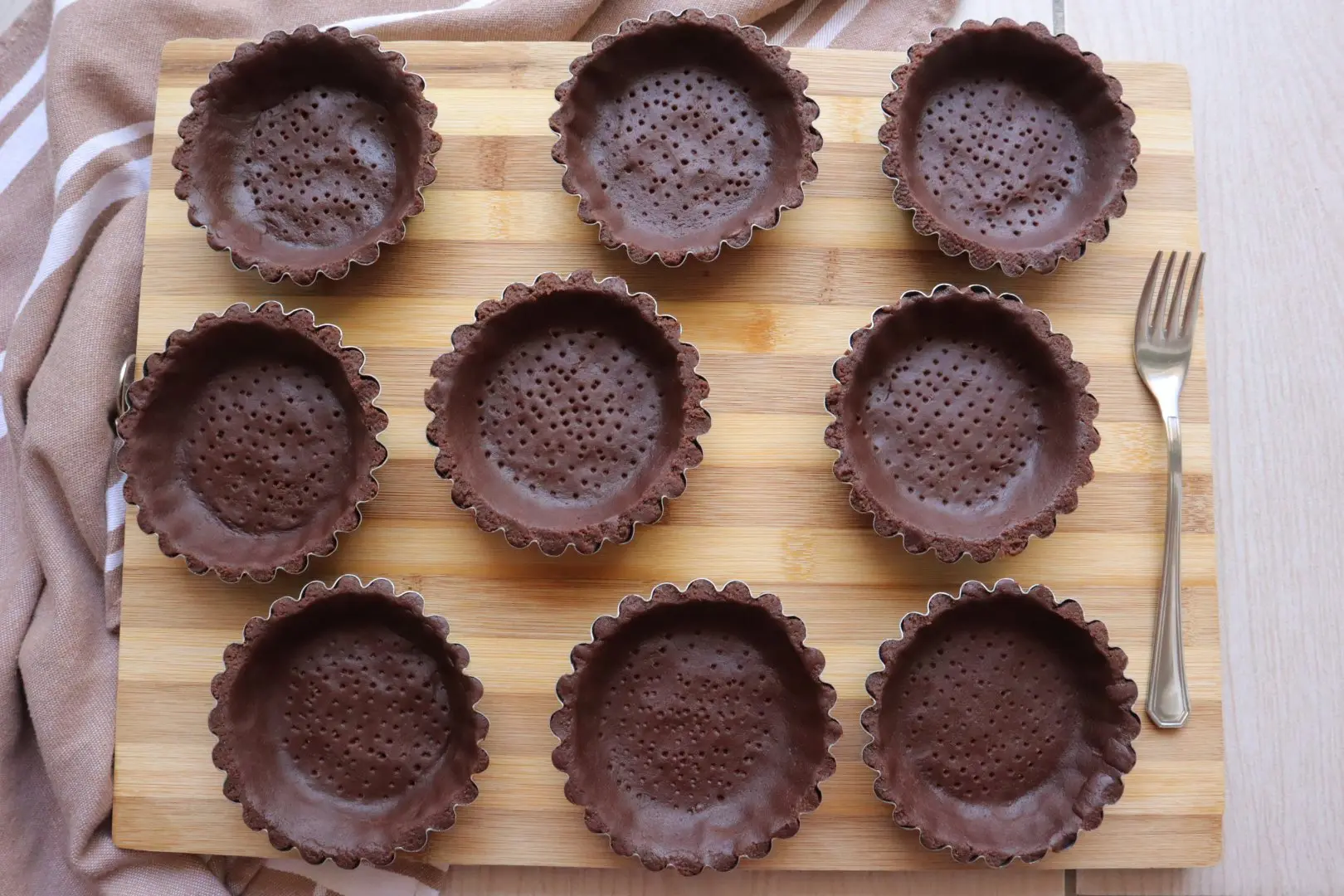 Tagliere di legno con tartellette al cioccolato pronte per essere guarnite con una con ganache.