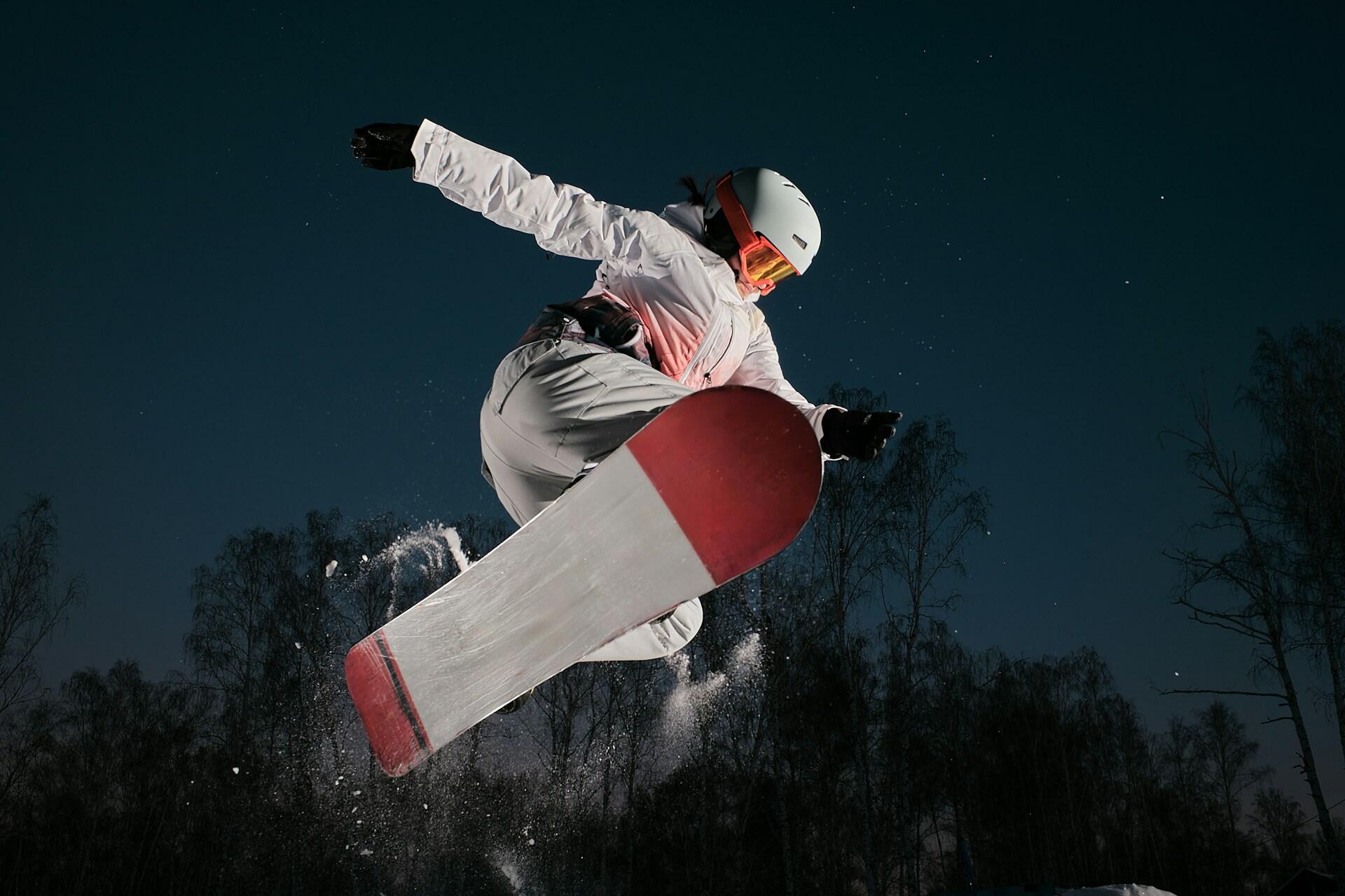Ragazza fa un salto con lo snowboard su una pista di notte. 