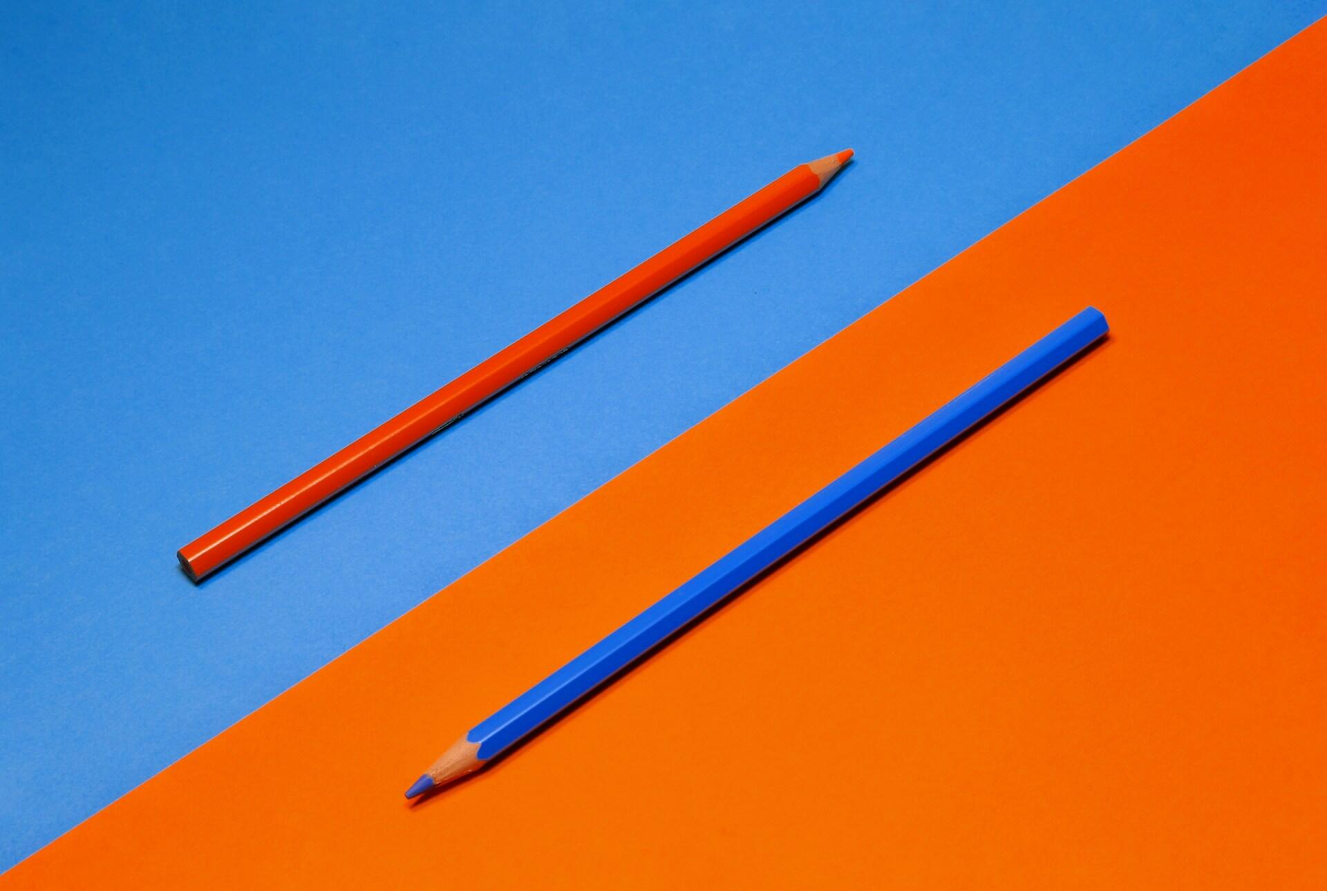 Un foglio diviso e metà con due matite di colori complementari, a indicare la staticità di un pareggio. 