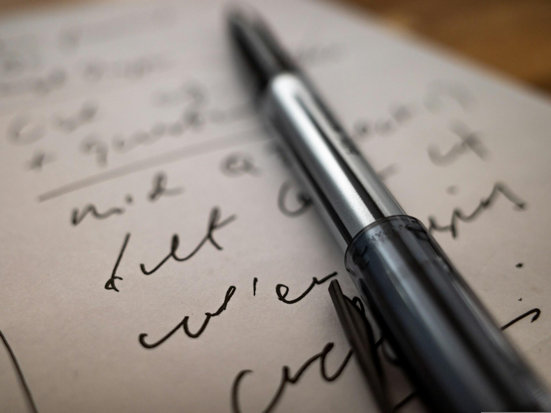 Penna poggiata su un foglio su cui si intravede scritta in corsivo. 