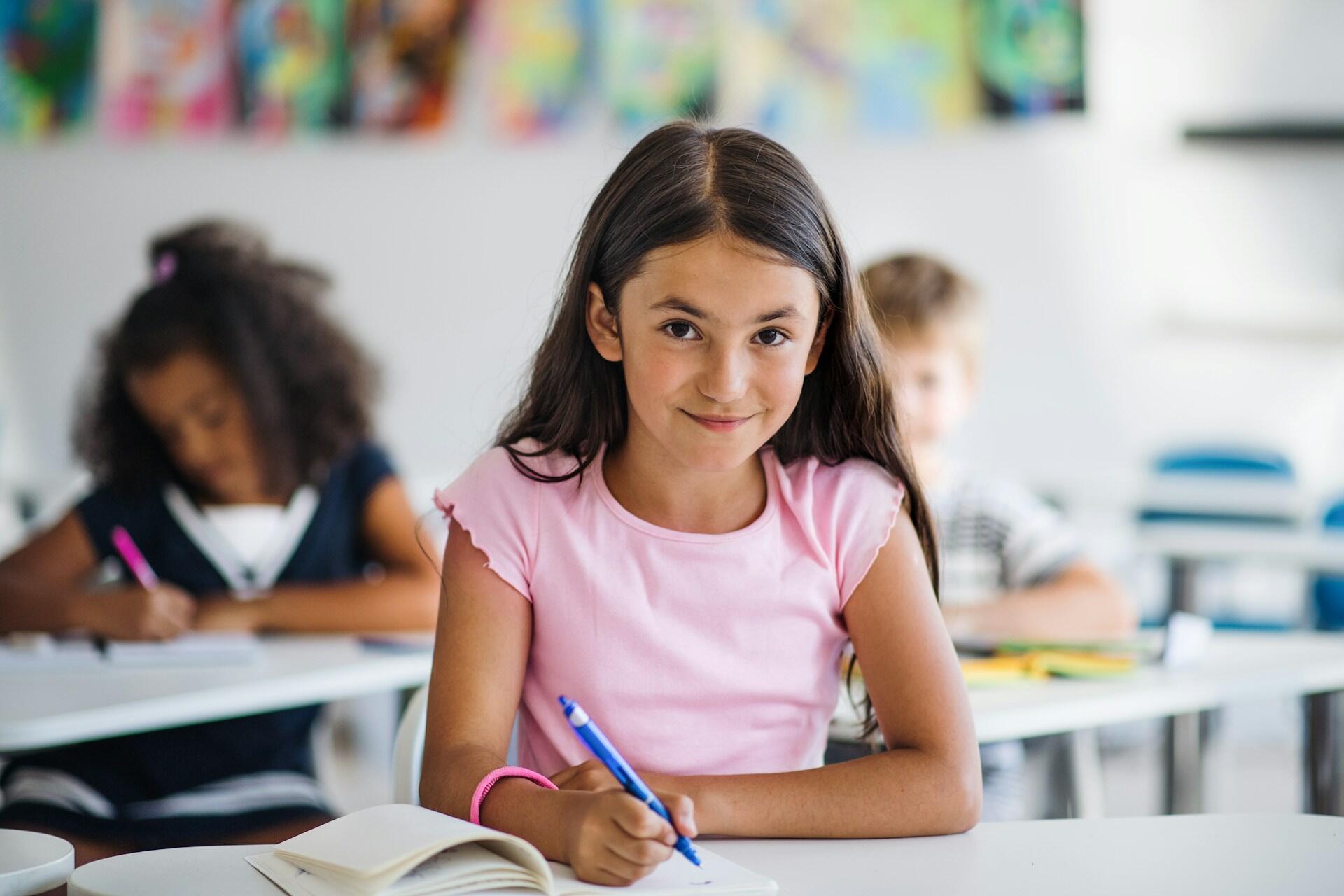Bambina di quarta elementare sorride mentre è intenta a svolgere un esercizio di analisi grammaticale.