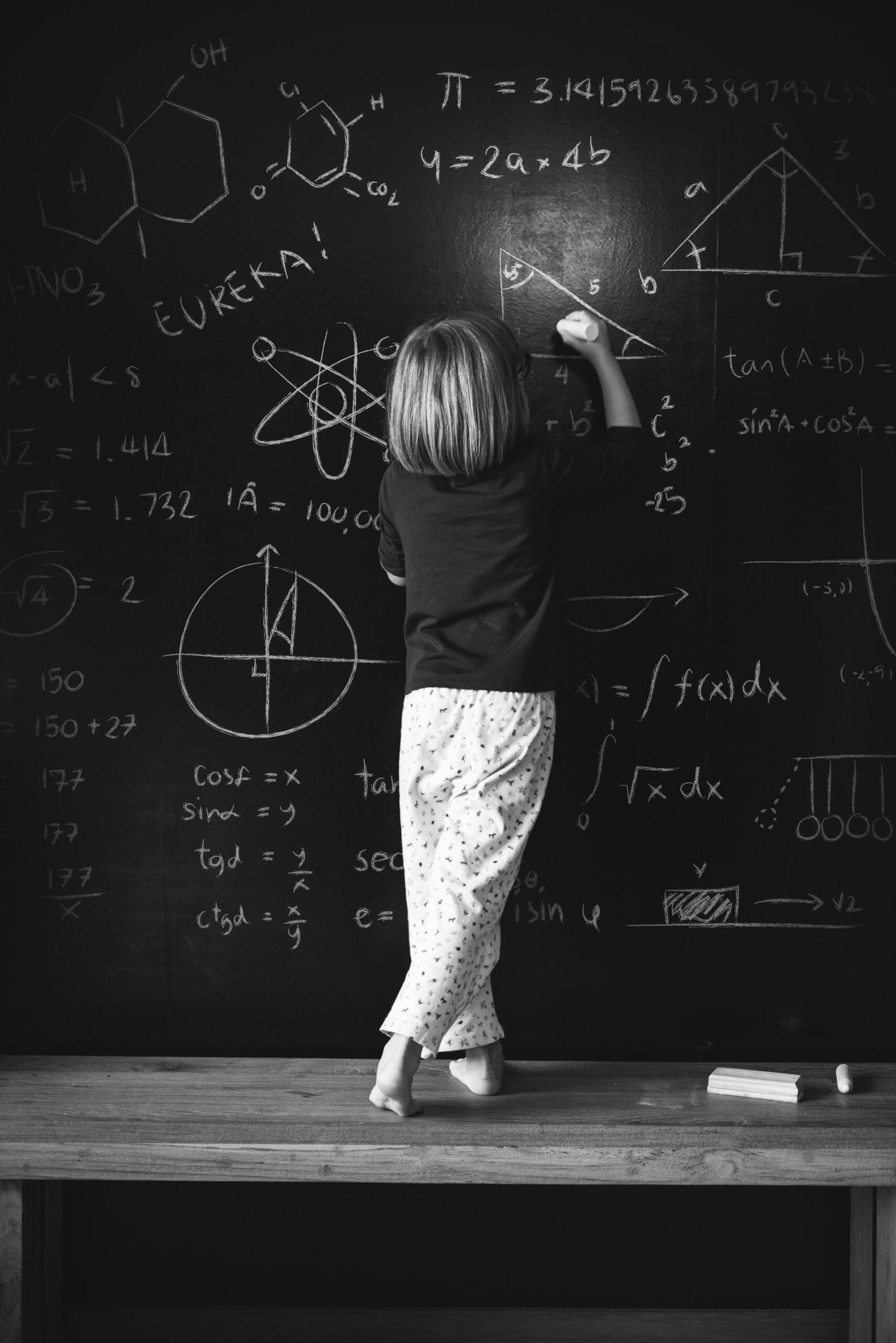 Bambino scrive formule matematiche su una lavagna.