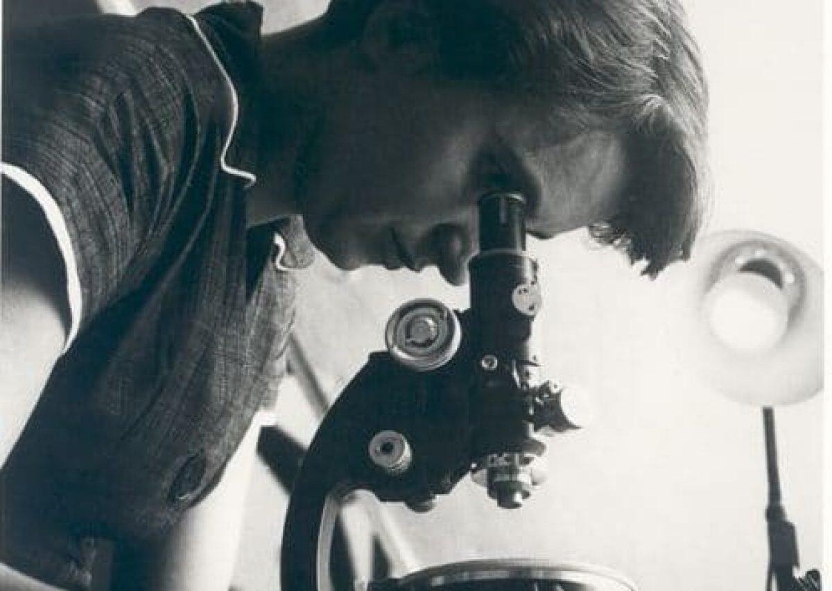 Immagine di Rosalind Franklin al microscopio, scienziata fondamentale per la scoperta della struttura del DNA e lo sviluppo della biologia molecolare.