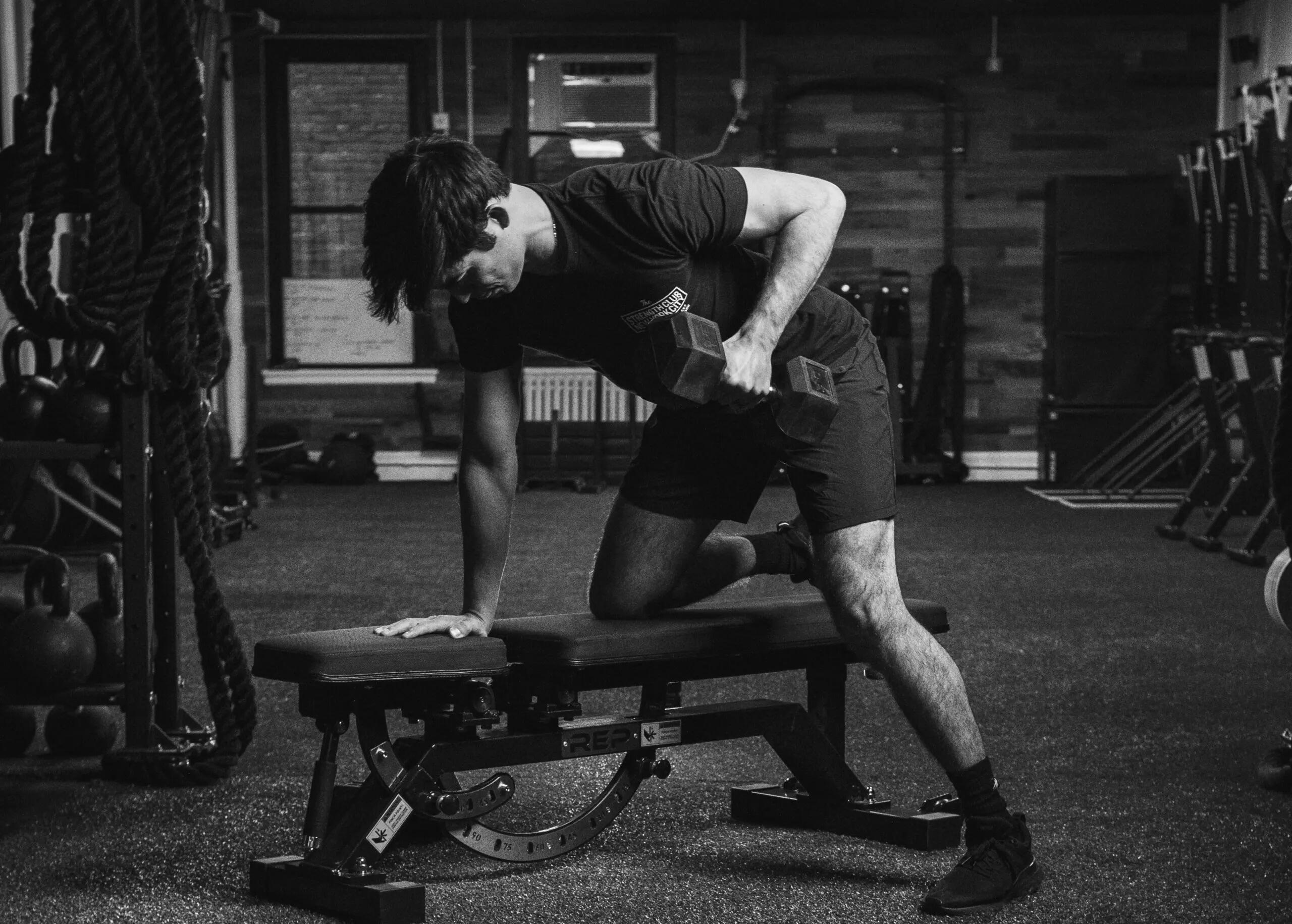 Un ragazzo si allena in una piccola palestra con manubri e panca.