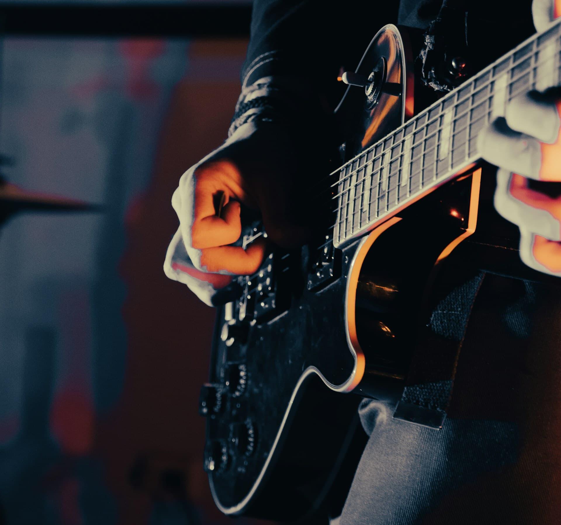黒いエレキギターをピックで弾くギタリスト
