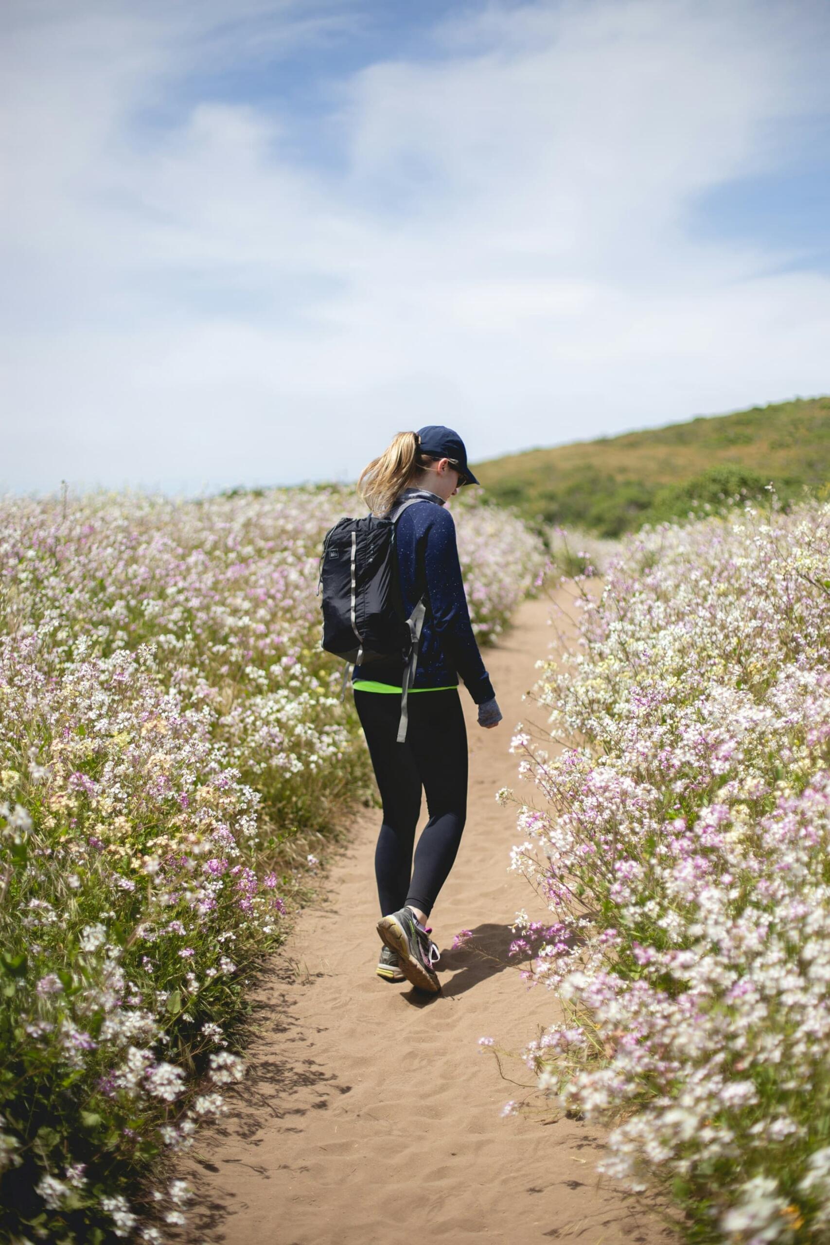 花の咲く小道をウォーキングする女性の後ろ姿