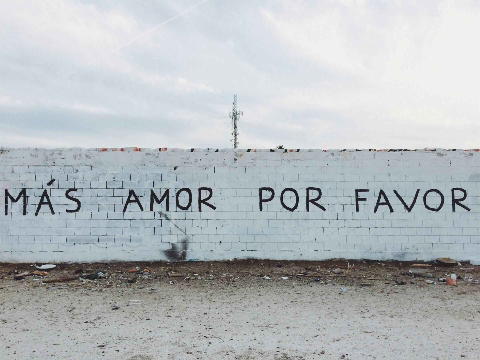 Užrašas ant baltos plytinės sienos "Mas amor por favor"