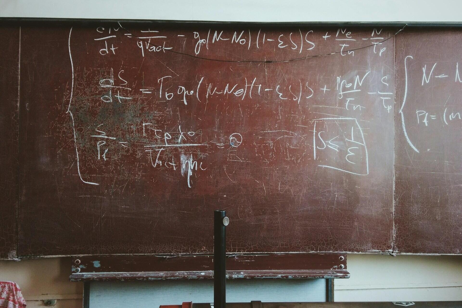 Ruda mokyklinė lenta su matematikos užduotimi parašyta balta kreida