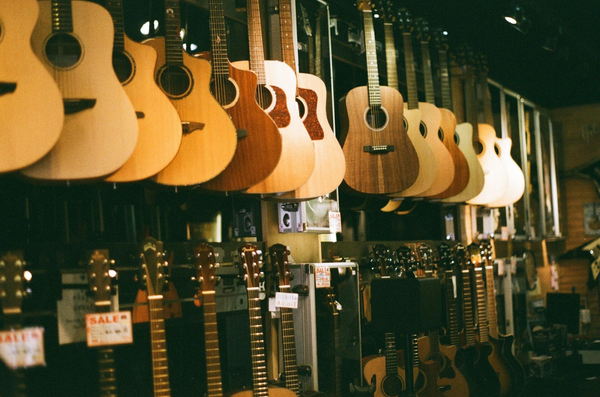 Klasikinės ir akustinės gitaros sukambintos ant sienos parduotuvėje.