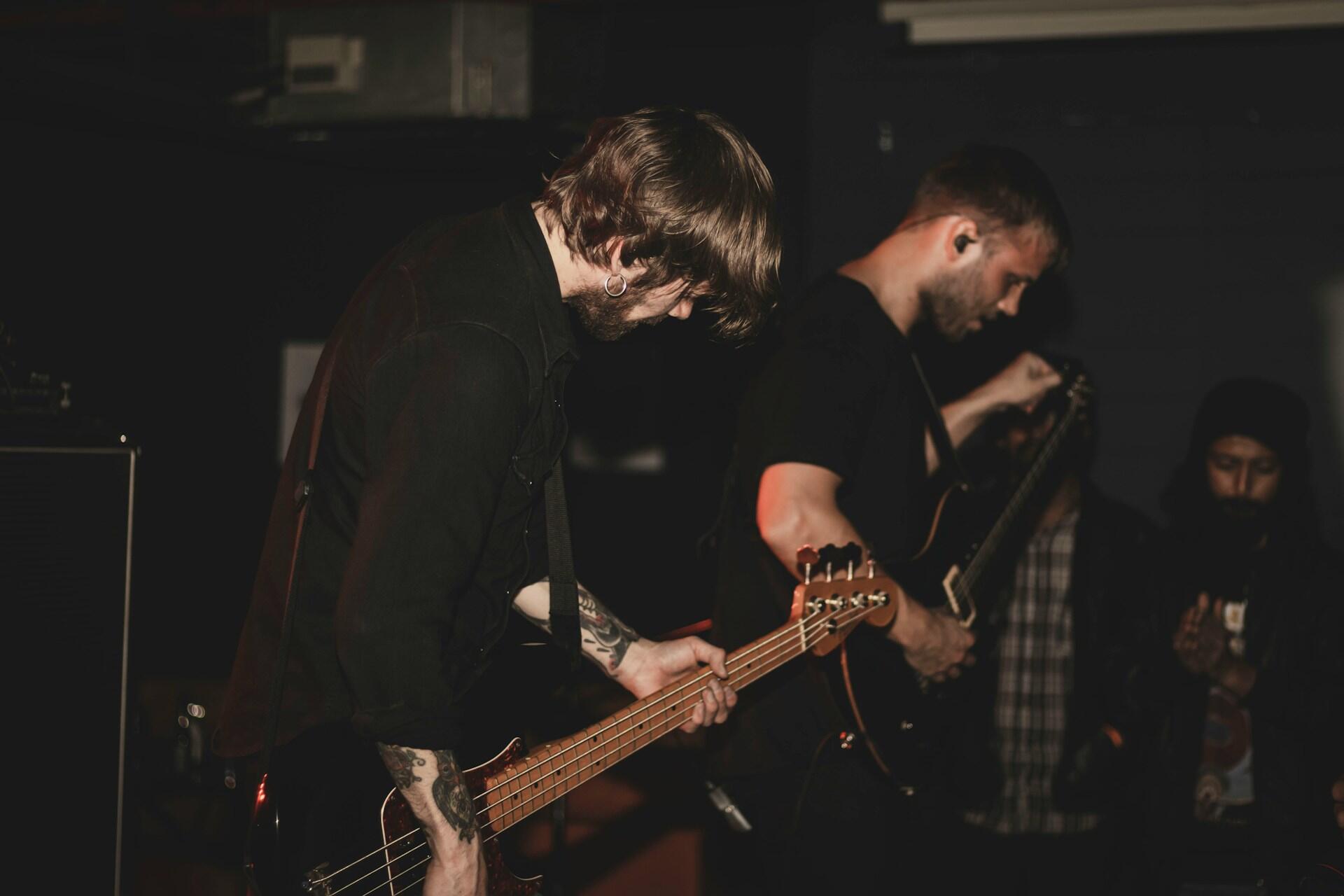 Du gitaristai ant scenos, viens iš jų derina gitarą.